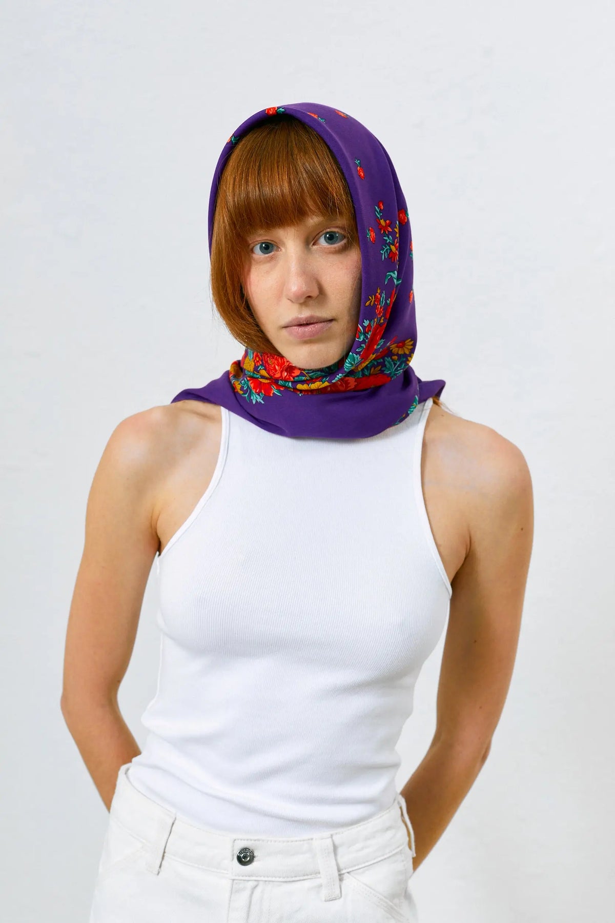 Pañuelo morado de estilo tradicional con estampado de flores coloridas, anudado en la cabeza sobre mujer joven.