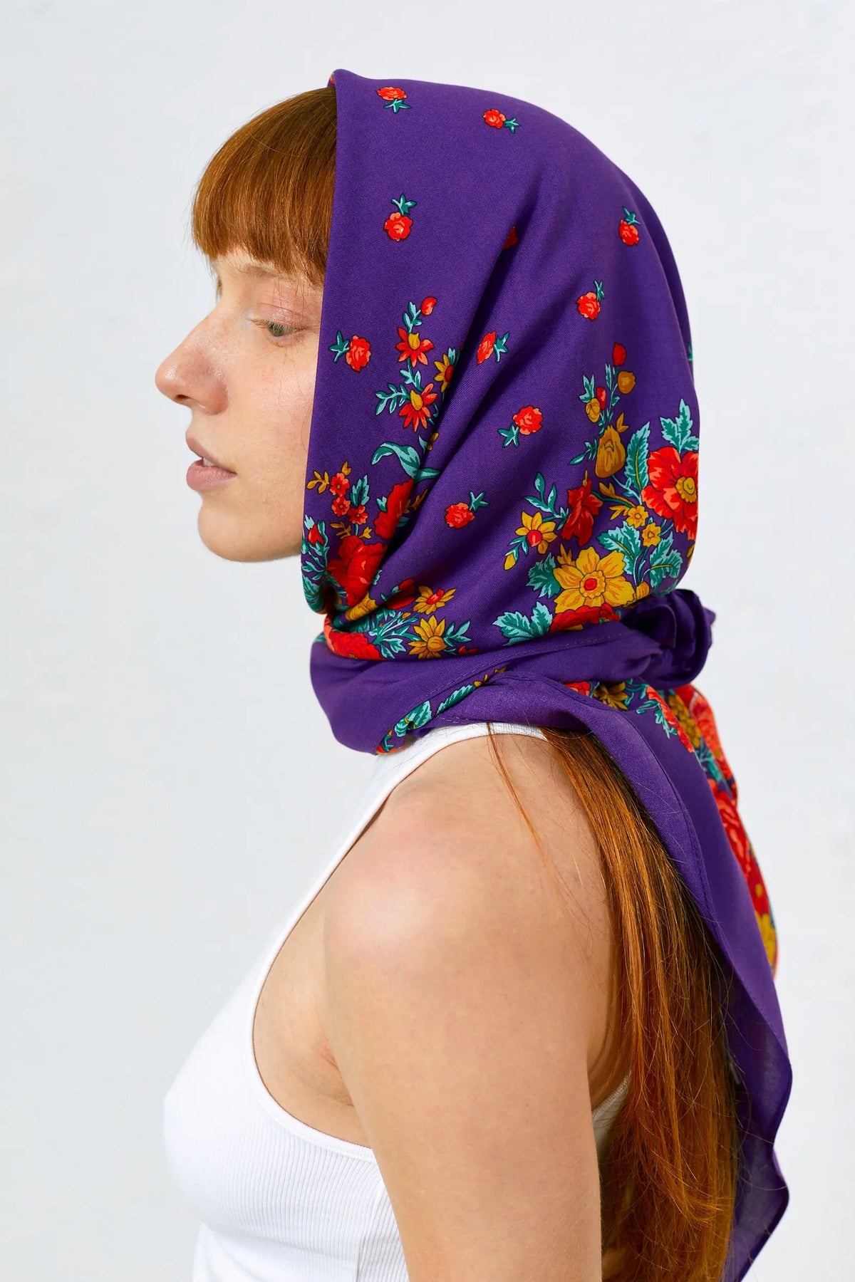 Mujer con pañuelo portugués morado estampado con flores rojas y amarillas atado a la cabeza. Estilo tradicional.