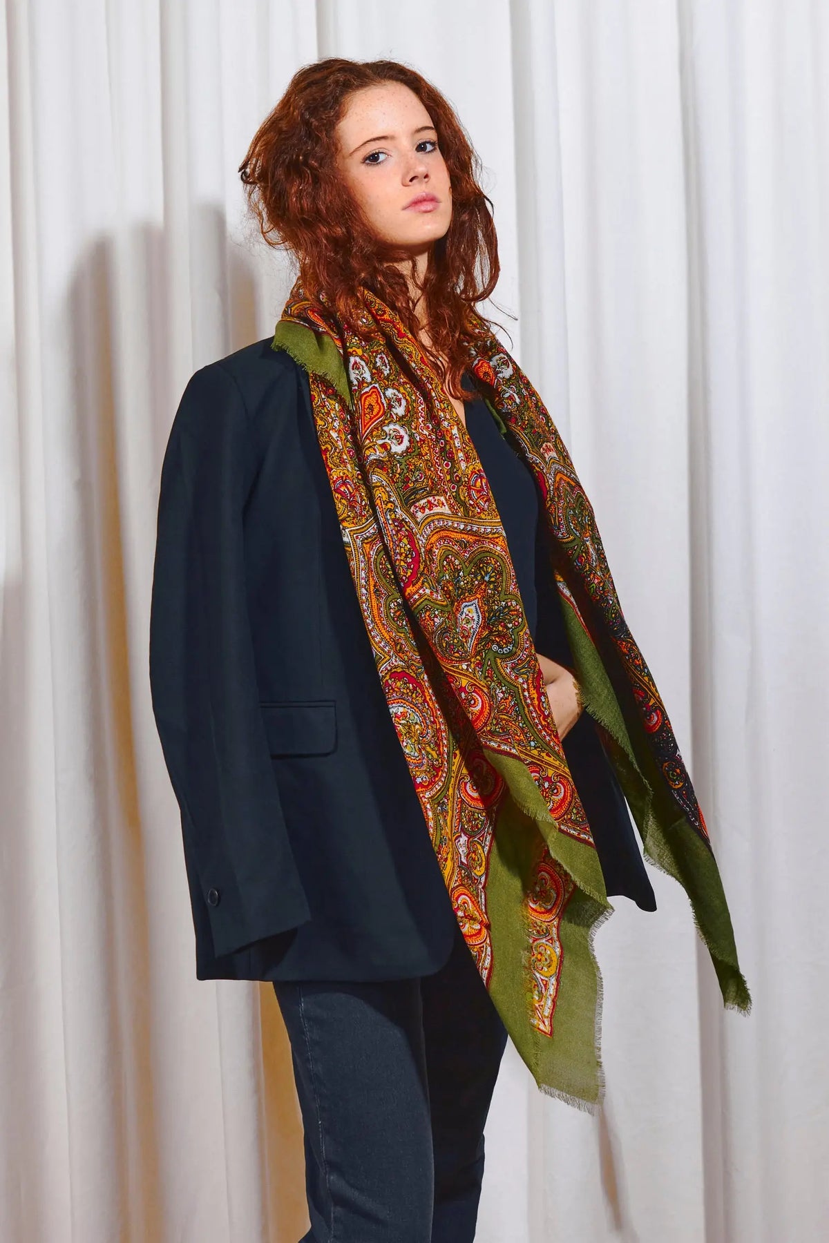Olive green wool scarf with a colorful paisley pattern worn over a dark blazer.