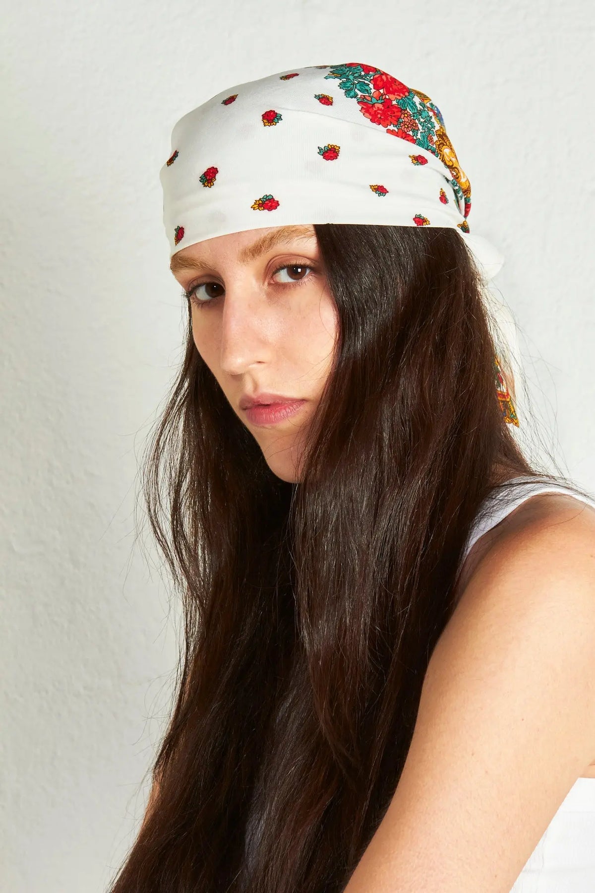 Woman wearing a white Portuguese-style headscarf with floral patterns and gold chain motifs on a white background.