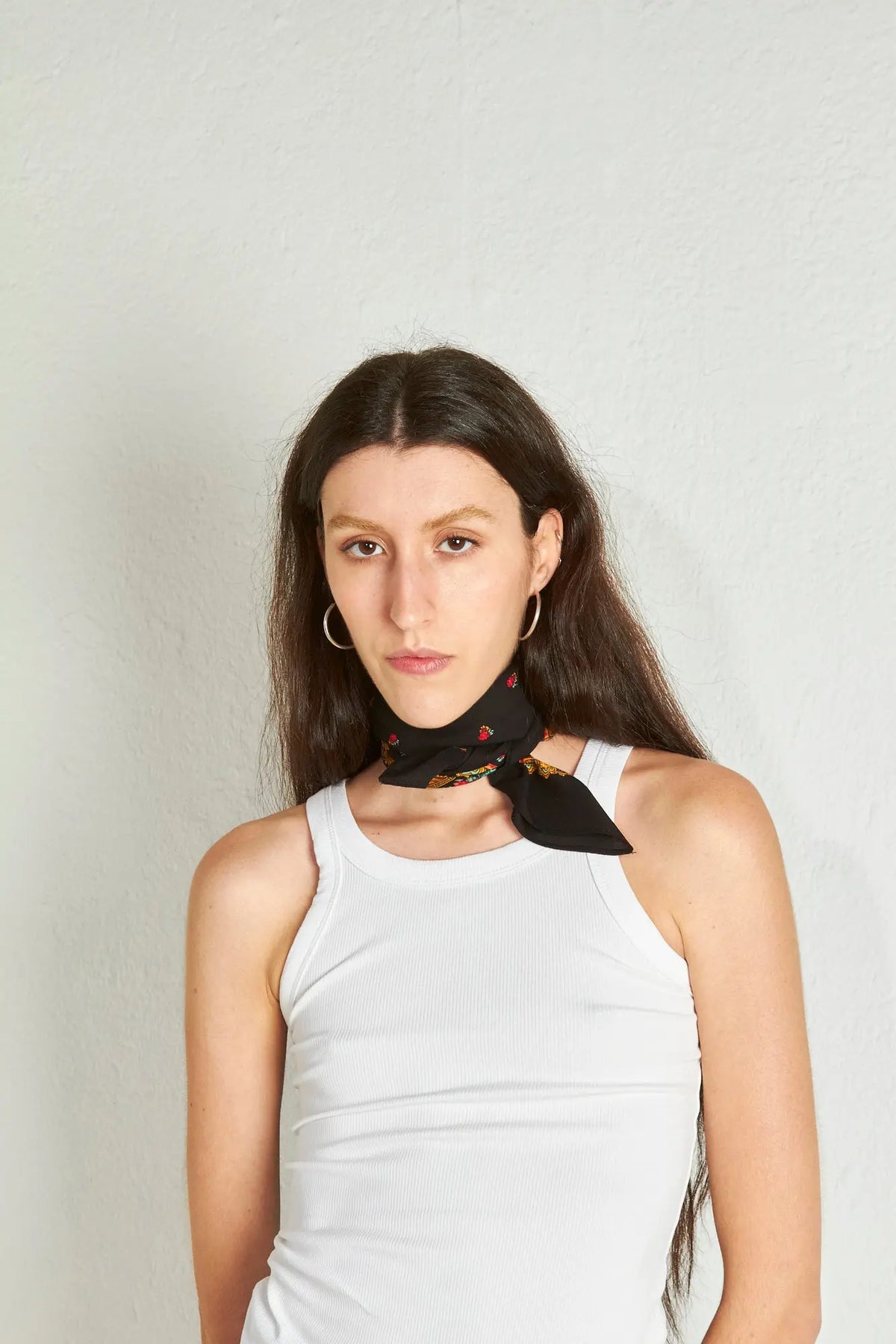 Mujer con pañuelo negro estilo portugués con estampado de cadenas y flores anudado al cuello sobre camiseta blanca.