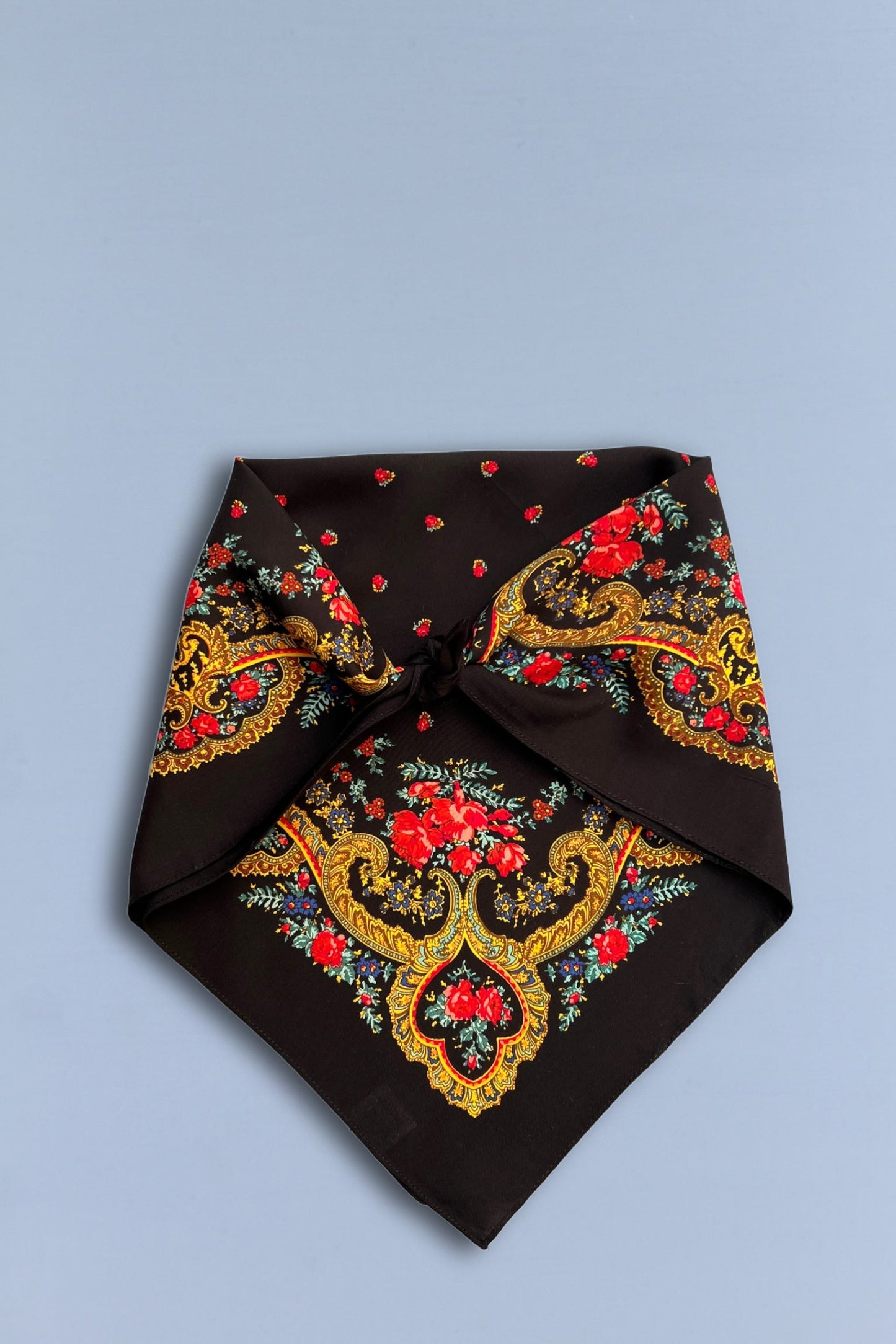 Pañuelo negro con estampado tradicional de flores rojas y motivos de cadenas doradas sobre fondo azul claro.