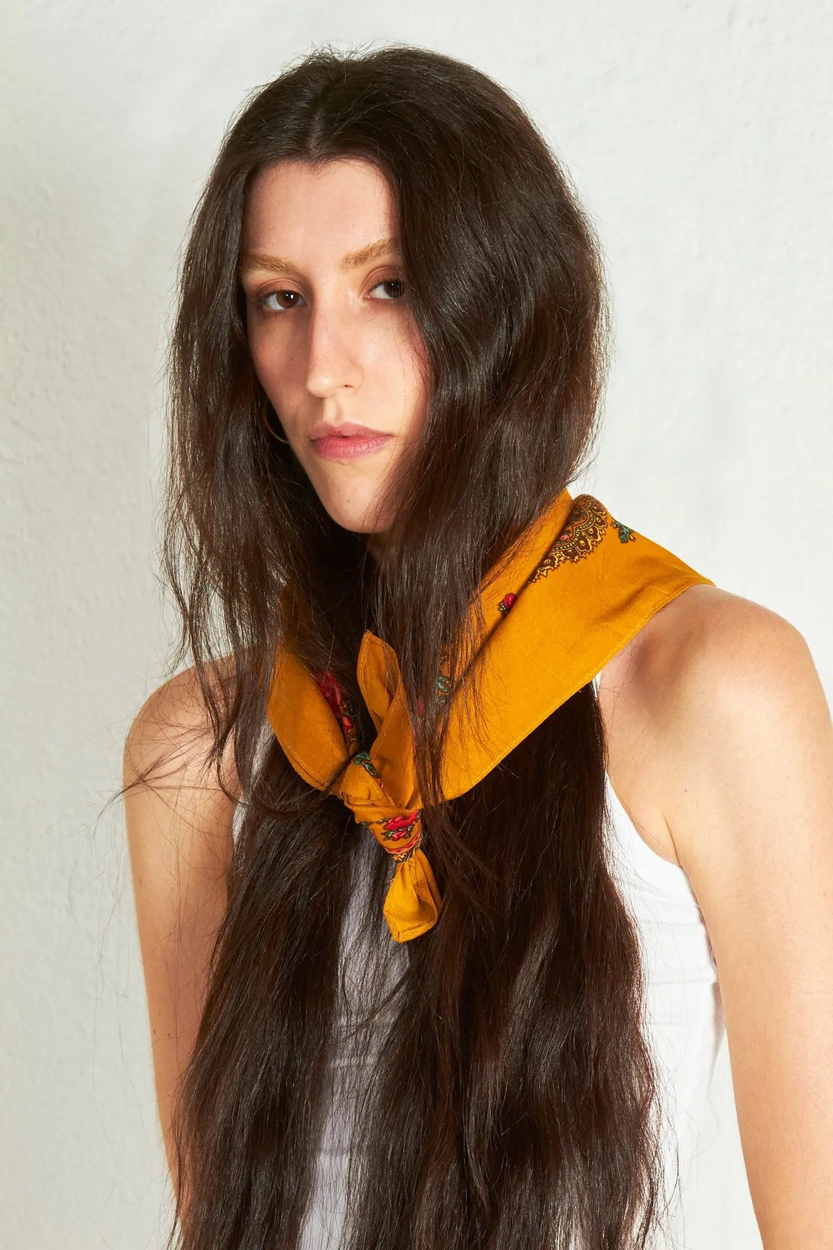 Woman wearing an ochre Portuguese-style neck scarf featuring a floral chain print, tied in a knot at the front.