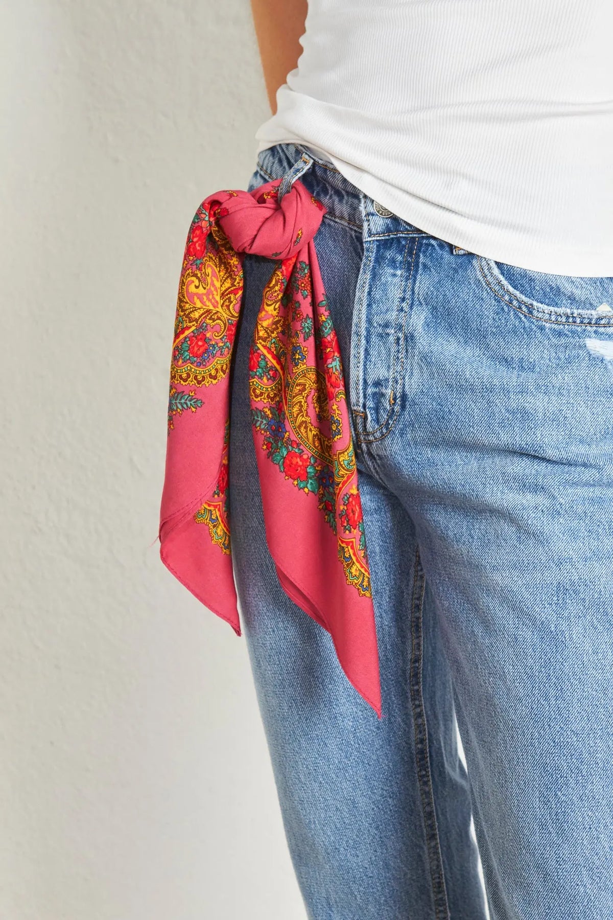 Pañuelo rosa con estampado floral y de cadenas atado en la trabilla de unos vaqueros azules.