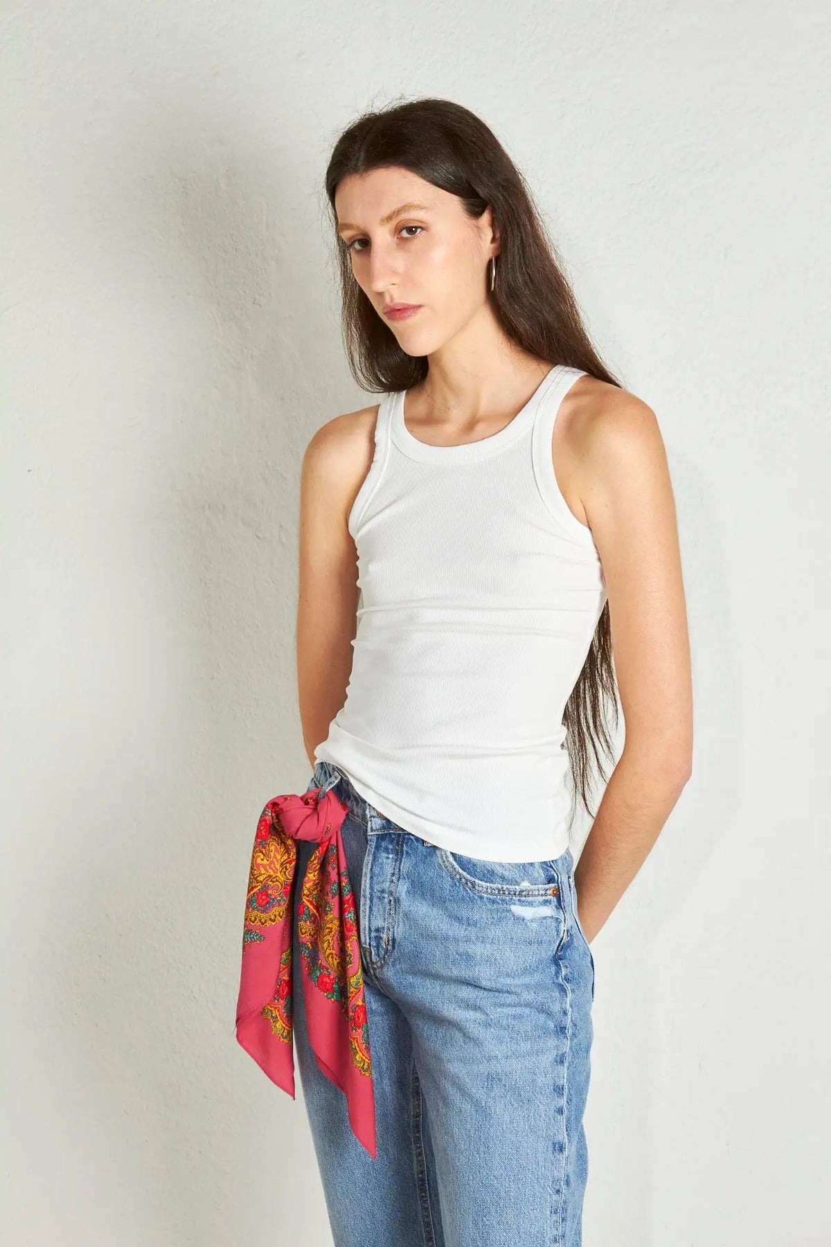 Pink scarf with traditional gold chain print, tied at the waist of blue jeans and a white tank top.