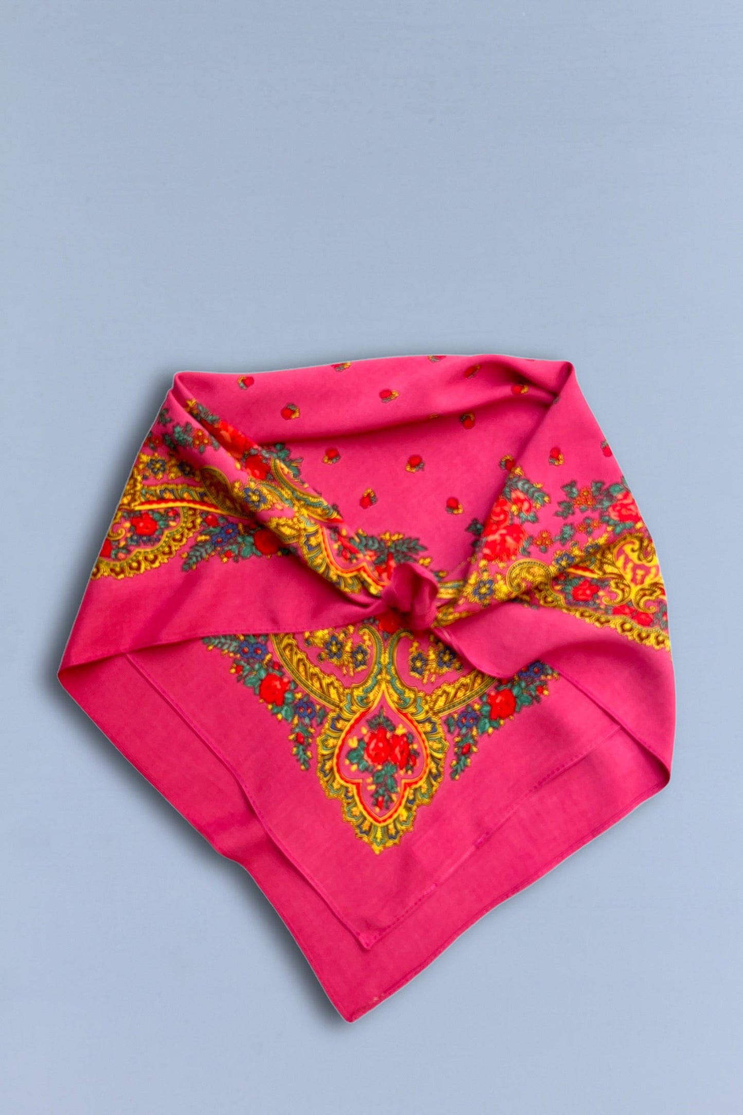 Pañuelo rosa estilo portugués con estampado de flores y cadenas doradas sobre fondo azul claro.