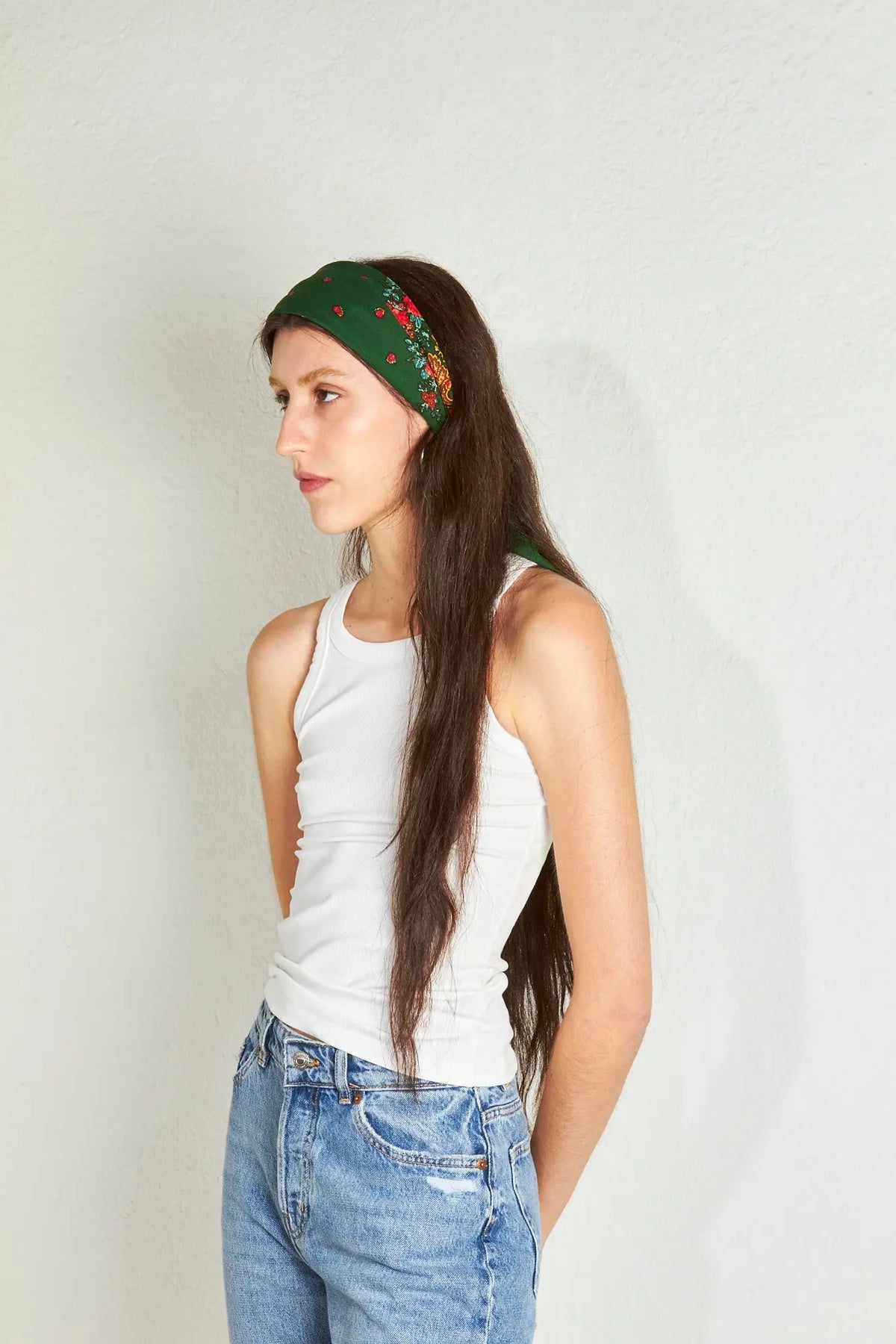Pañuelo verde botella con estampado floral y cadenas, estilo portugués, anudado en la cabeza sobre mujer joven.
