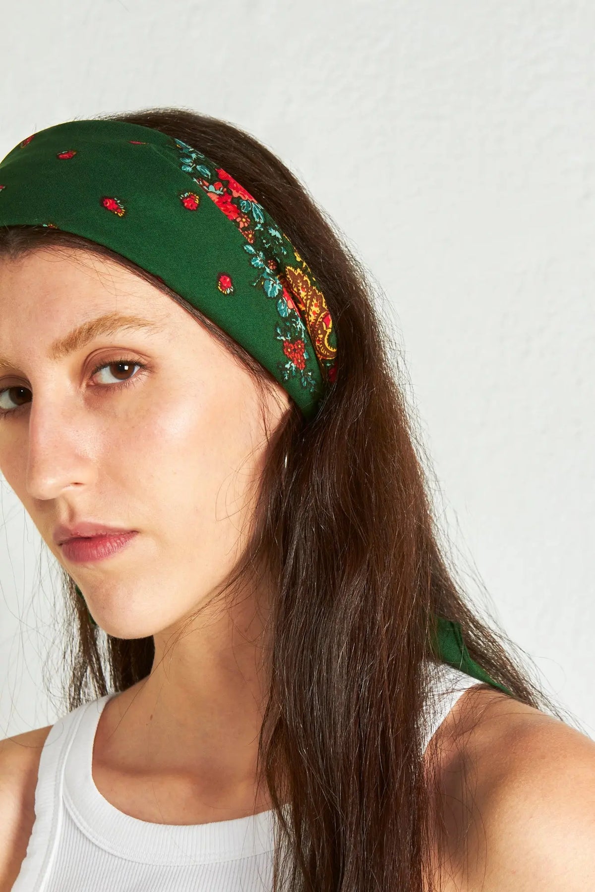 Pañuelo verde botella tipo portugués con estampado floral y de cadenas, colocado como diadema en el cabello.