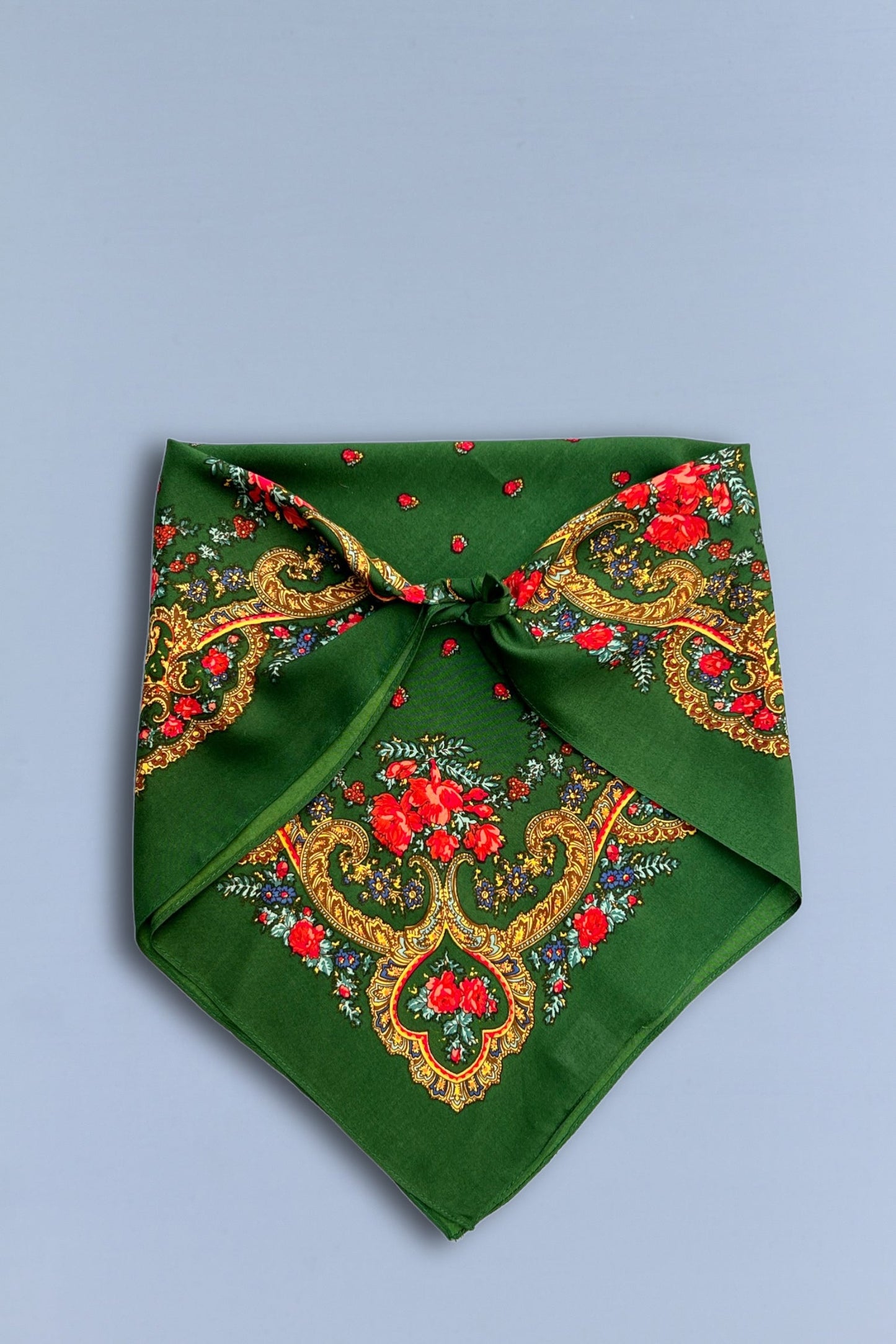 Pañuelo verde botella con estampado floral, motivos de cadenas doradas y estilo clásico sobre fondo gris.