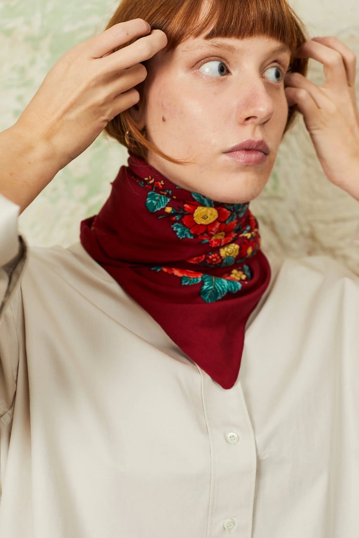 Pañuelo de estilo portugués en color granate con estampado de flores coloridas, atado al cuello de una mujer.