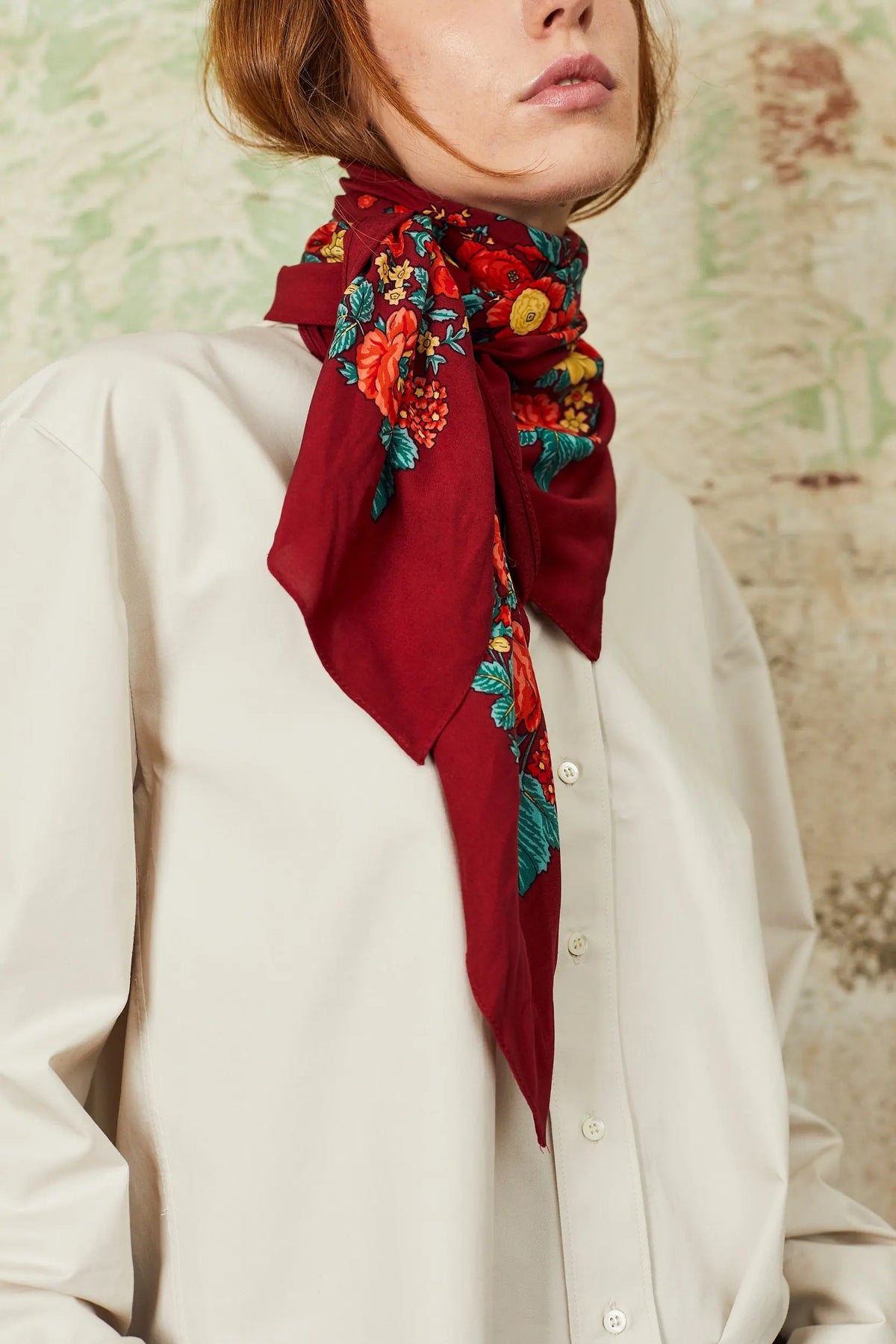 Woman wearing a square burgundy Portuguese scarf with vibrant red, yellow, and teal floral print, tied at the neck.