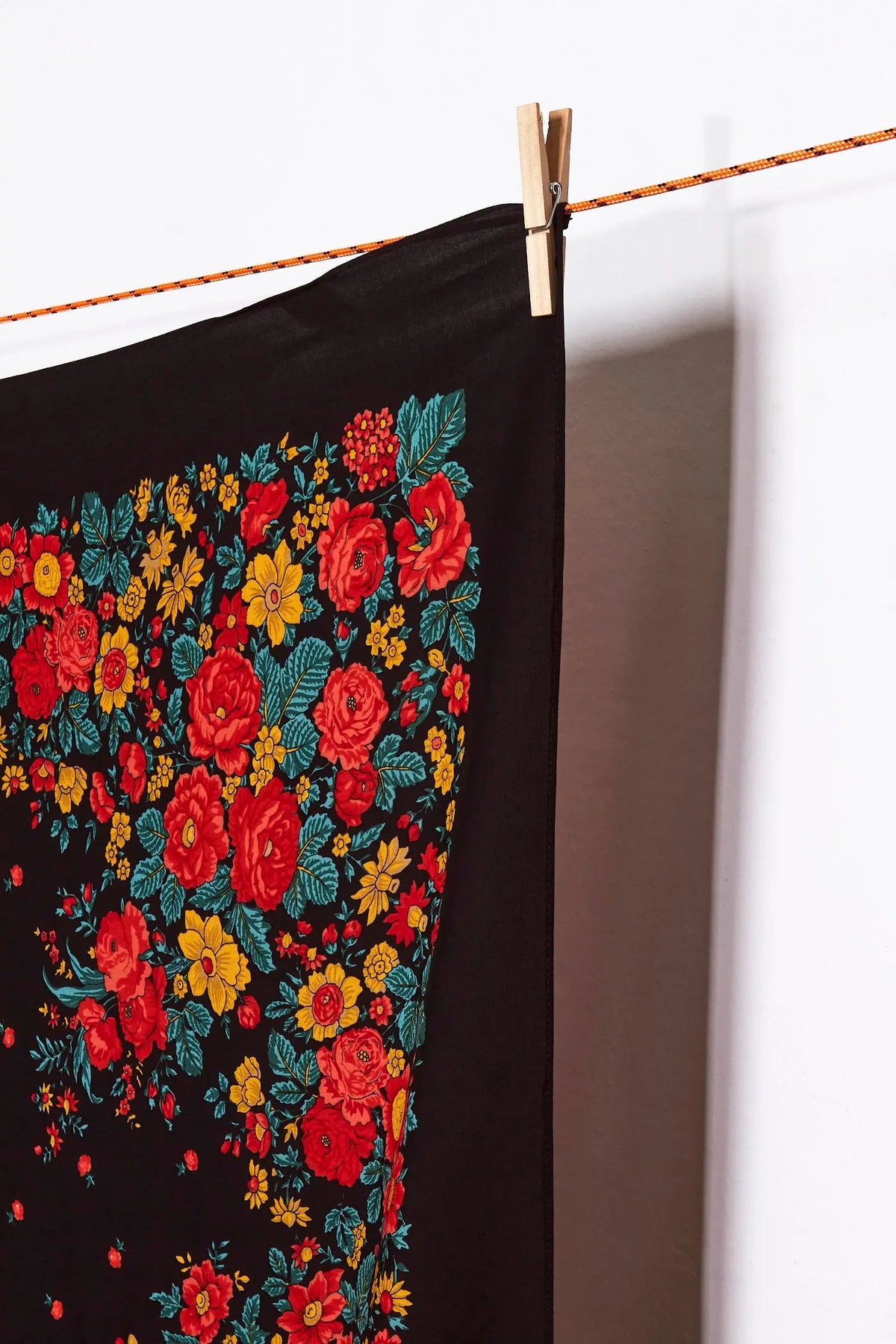 Pañuelo negro con estampado floral colorido de estilo tradicional colgado de una cuerda con una pinza de madera.