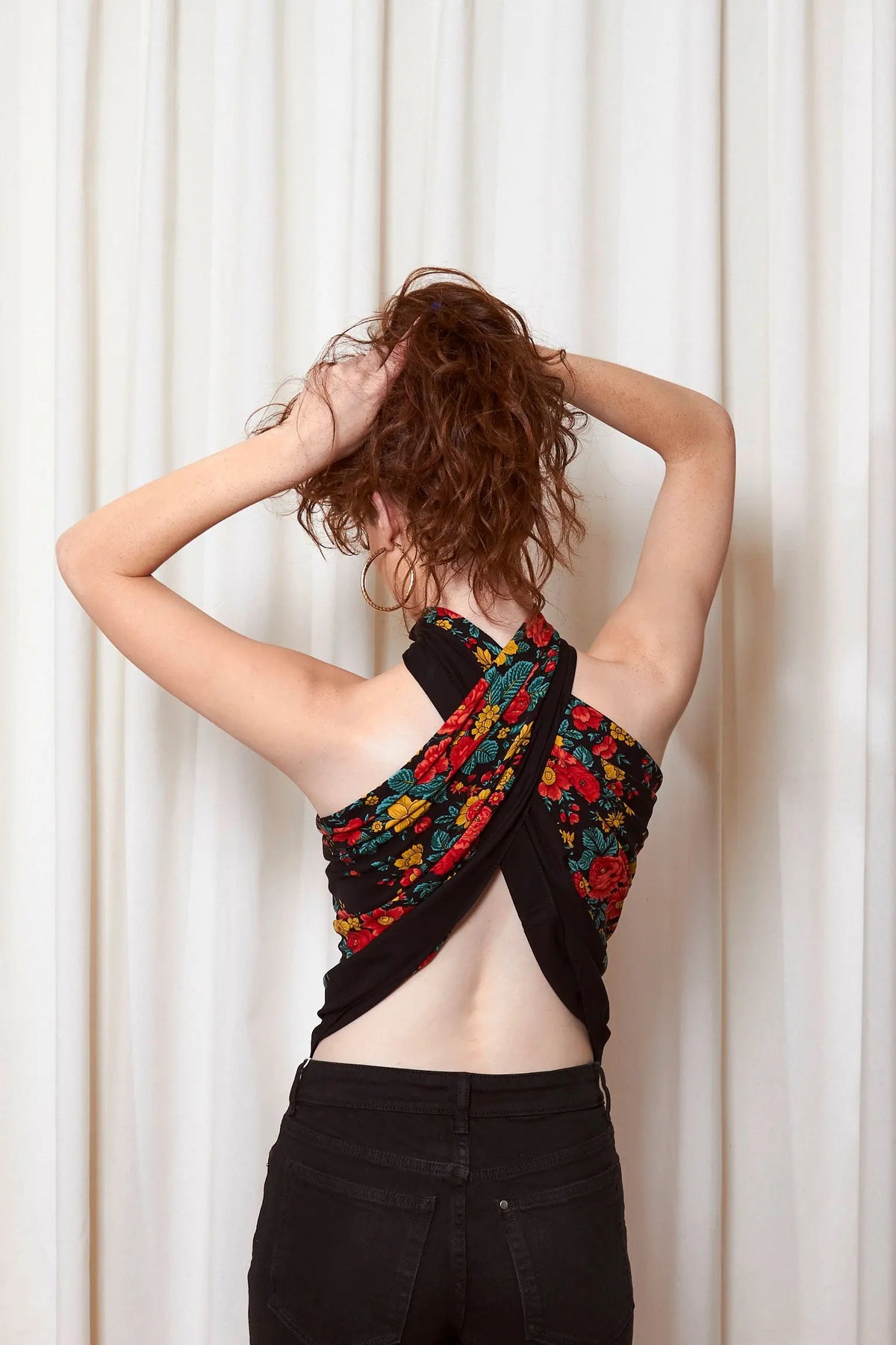 Pañuelo negro con estampado floral colorido usado como top cruzado en la espalda sobre fondo blanco.