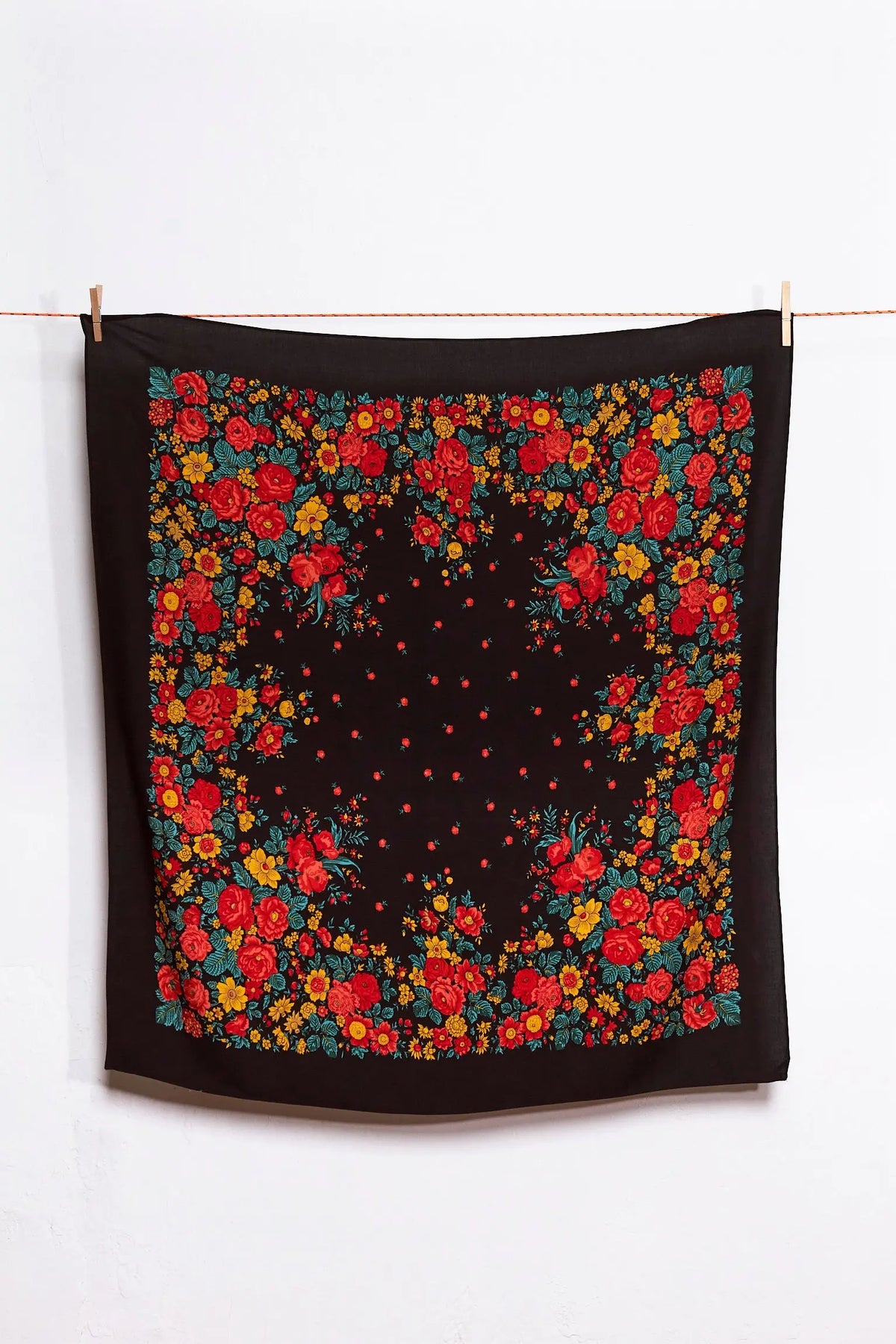 Pañuelo cuadrado negro con estampado tradicional de flores rojas, amarillas y verdes, colgado de una cuerda.