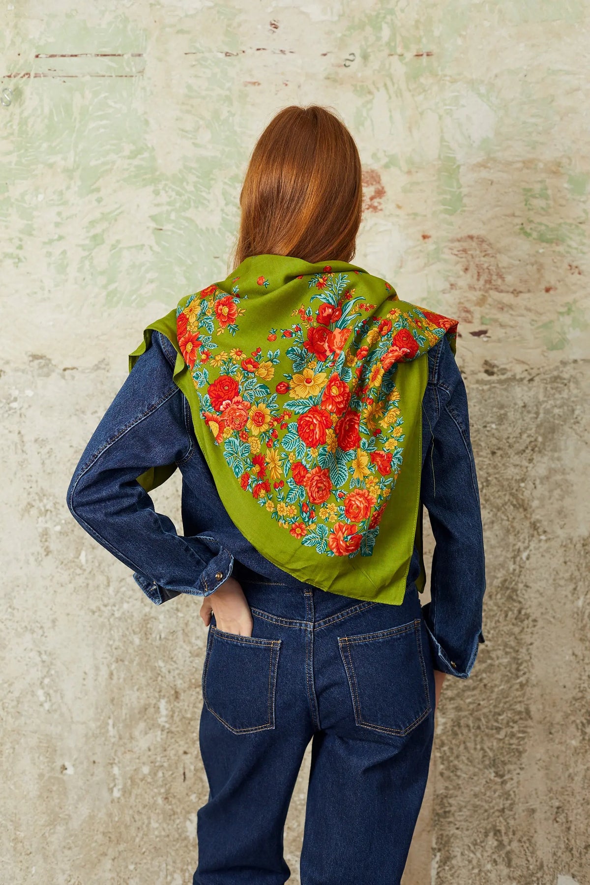 Olive green square scarf with vibrant red and yellow floral pattern, worn over a denim jacket and jeans.