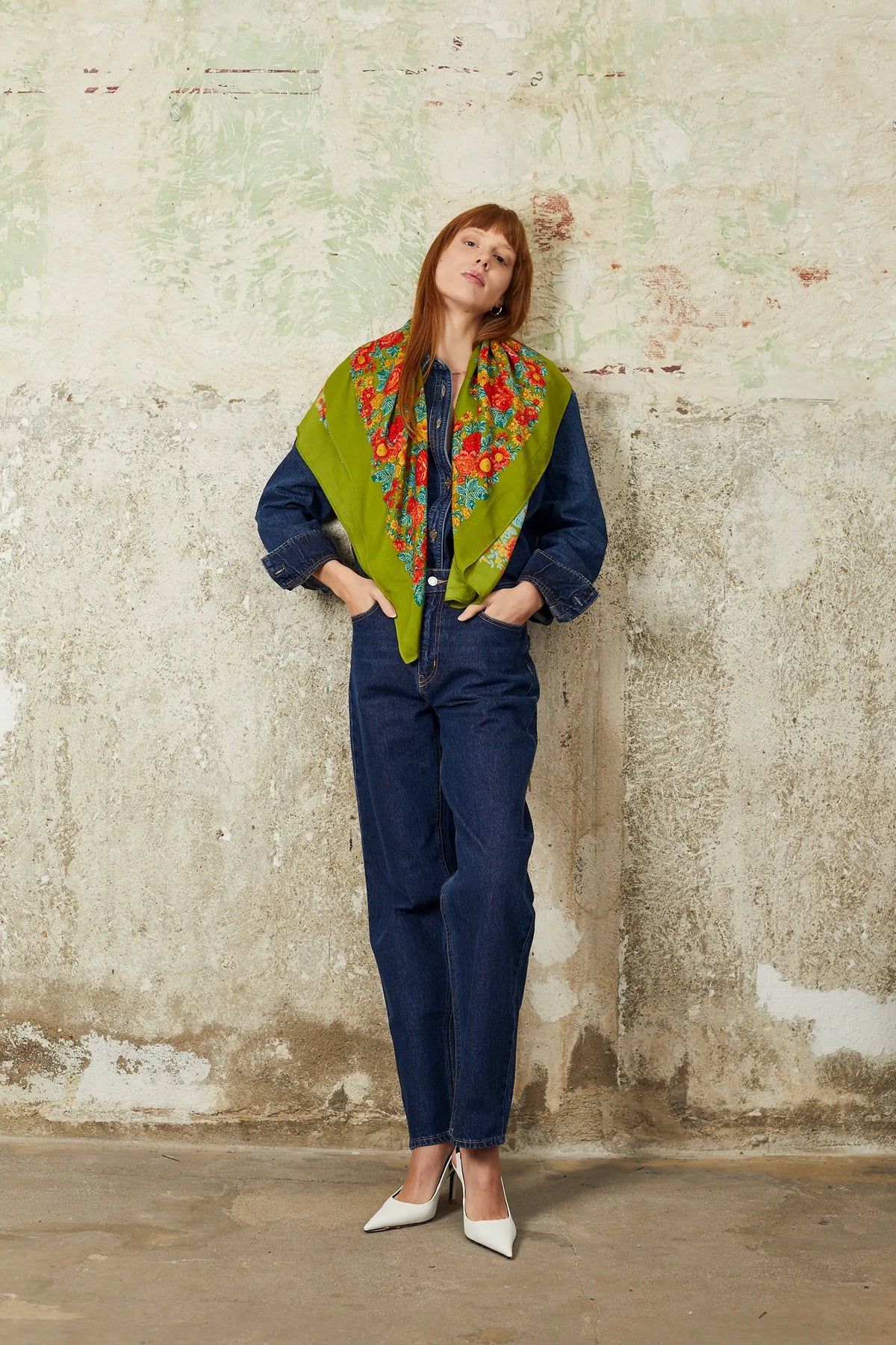 Olive green square scarf with vibrant red, orange, and blue floral patterns worn over a denim outfit.