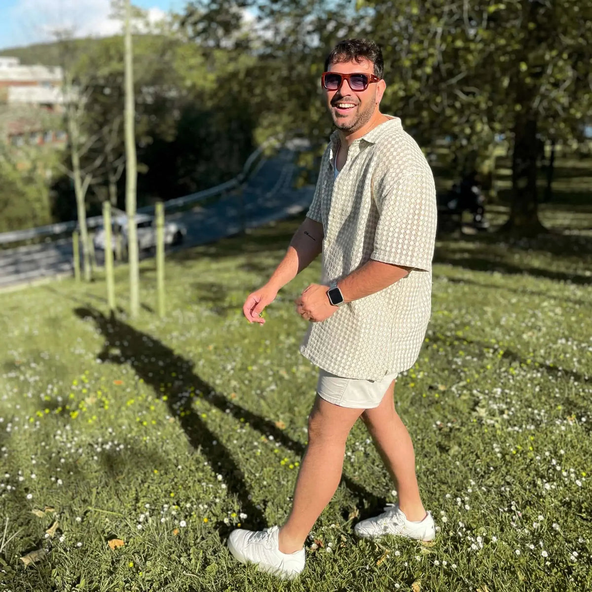 Hombre con camisa texturizada y gafas de sol cuadradas con montura de vetas de madera y lentes azules en un parque.