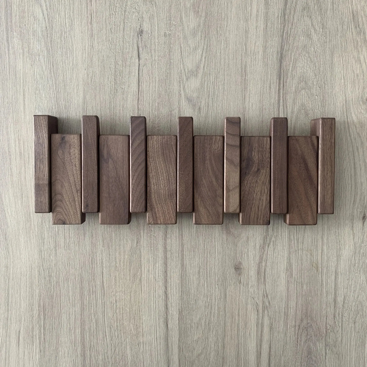 Perchero de pared de madera natural con diseño plegable escandinavo de listones verticales en tonos marrón oscuro.