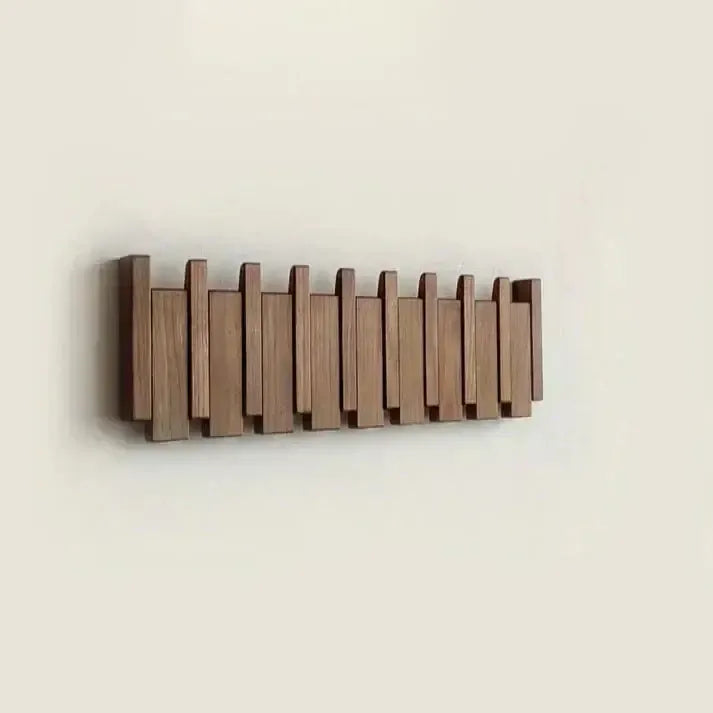 Perchero de pared estilo escandinavo, hecho de listones de madera natural plegables en tono marrón sobre fondo claro.