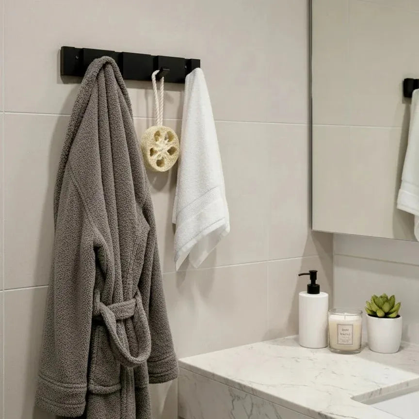 Perchero de pared moderno en metal negro con varios ganchos, instalado en un baño con albornoz y toalla colgados.