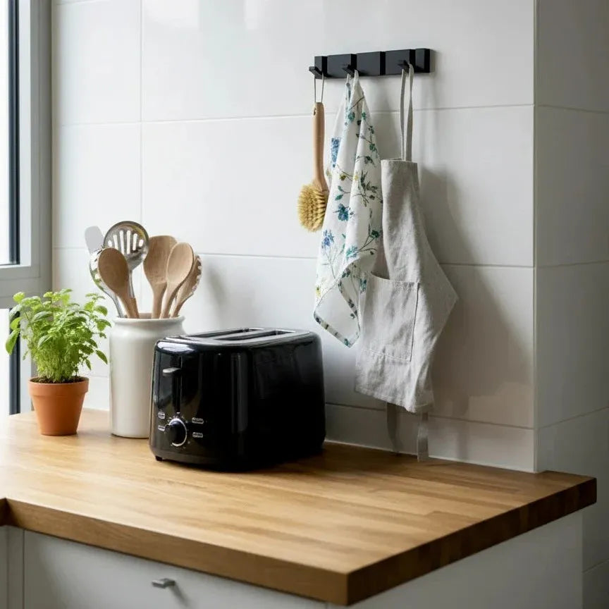 Perchero de pared moderno de metal negro con varios ganchos, instalado sobre azulejos blancos en una cocina.