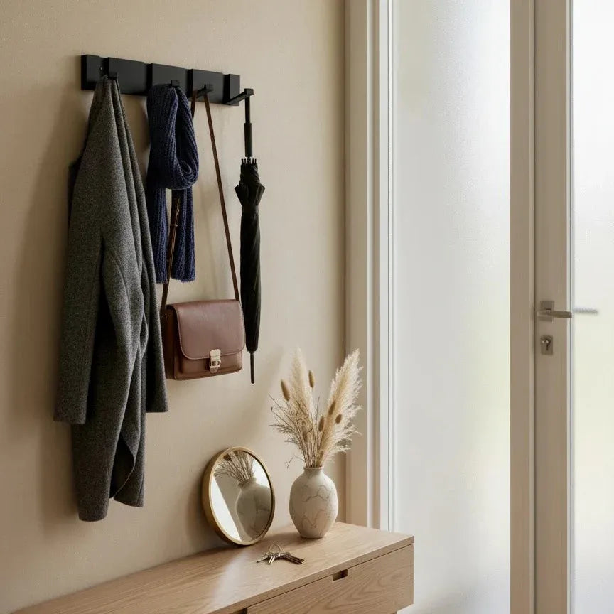 Perchero de pared moderno en metal negro con varios ganchos, sosteniendo abrigos y accesorios en una entrada minimalista.