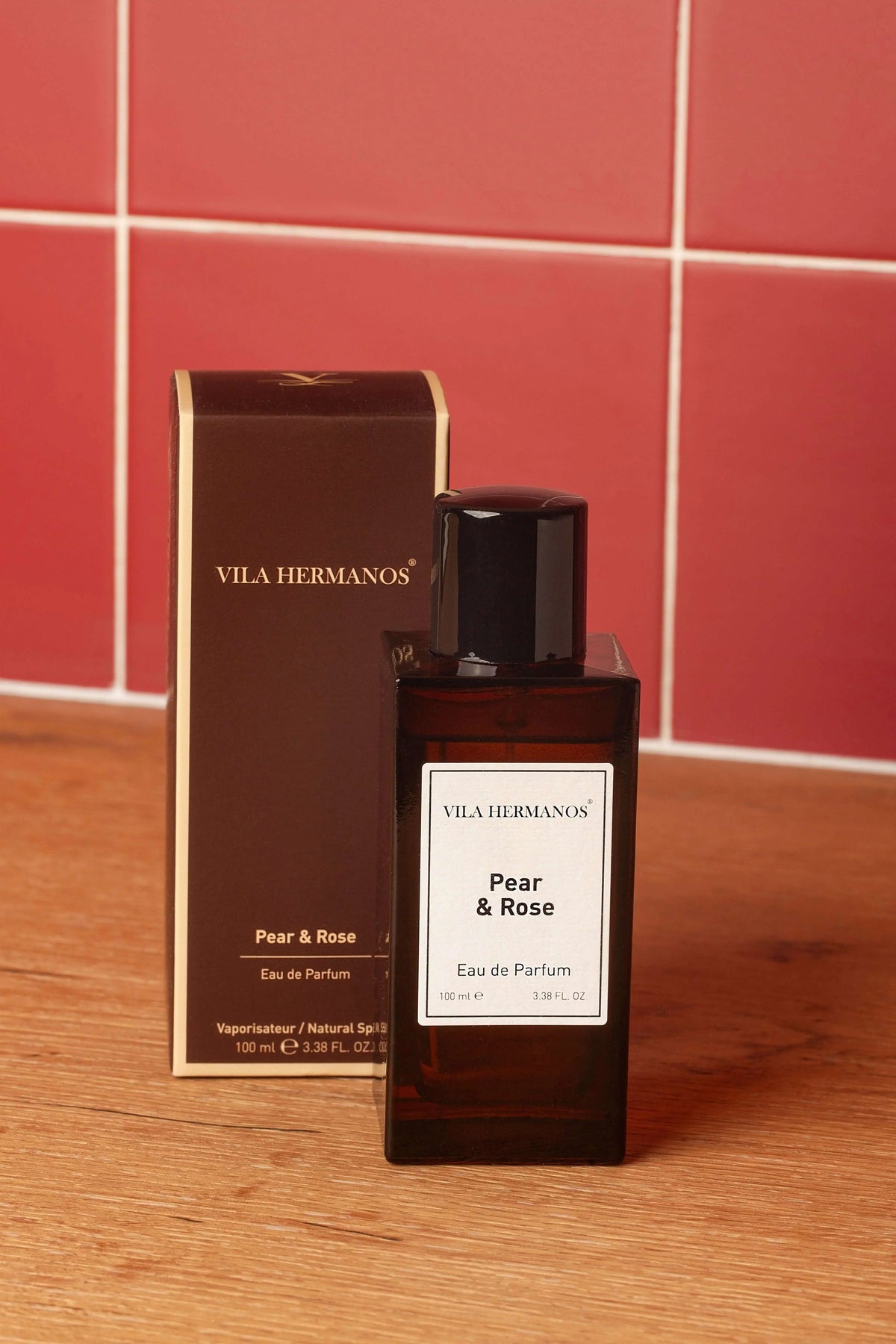 Vila Hermanos Pear & Rose perfume bottle and box in amber glass against a red tiled wall and wooden surface.