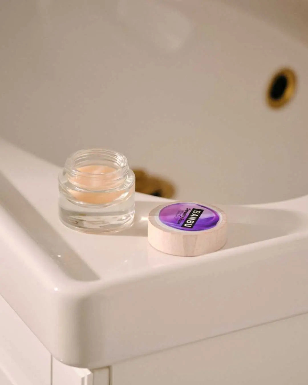 Perfume sólido Banbu en tarro de vidrio con tapa de madera sobre un lavabo blanco de estilo minimalista.