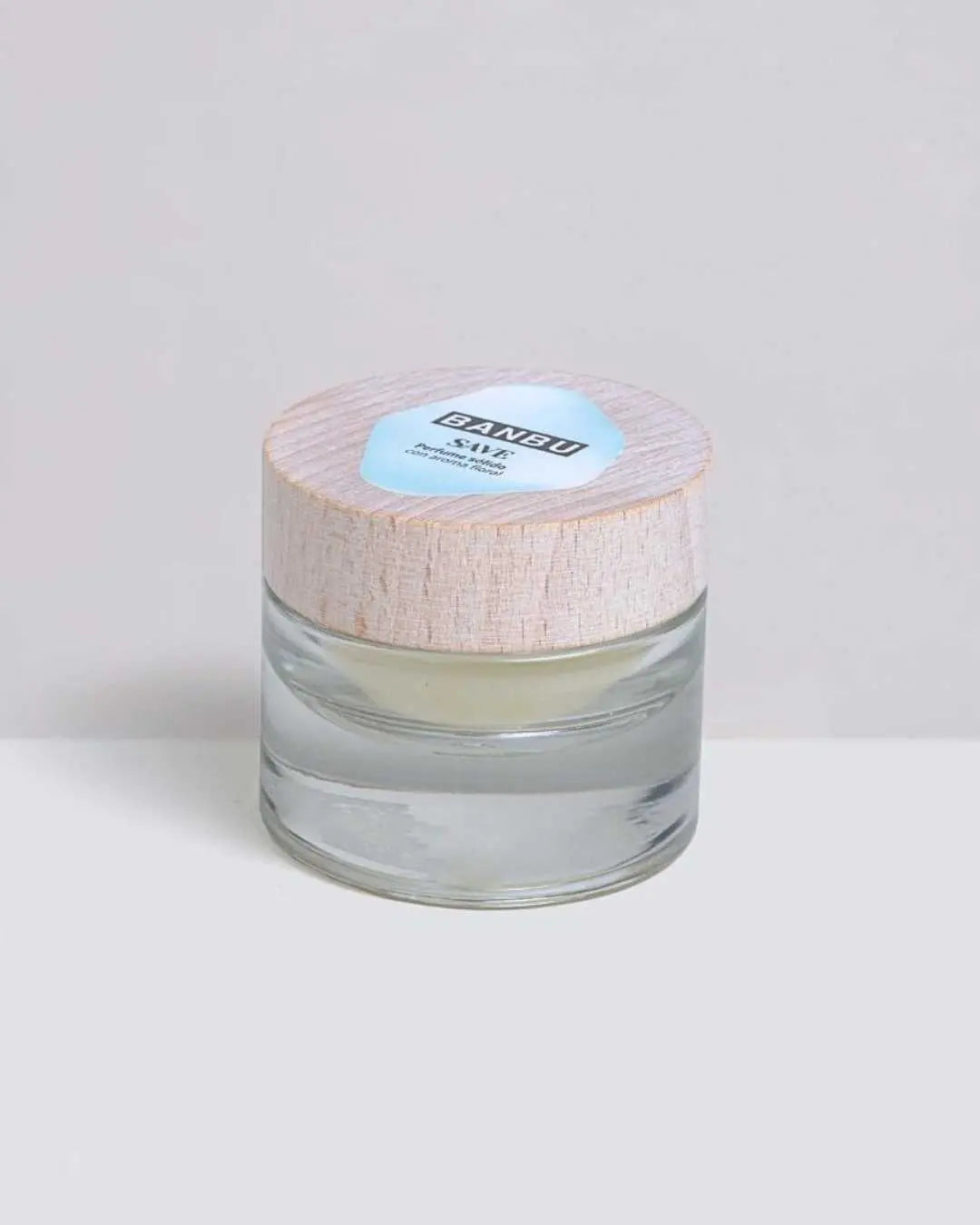 Perfume sólido Banbu SAVE en frasco de cristal con tapa de madera clara y etiqueta azul sobre fondo neutro.