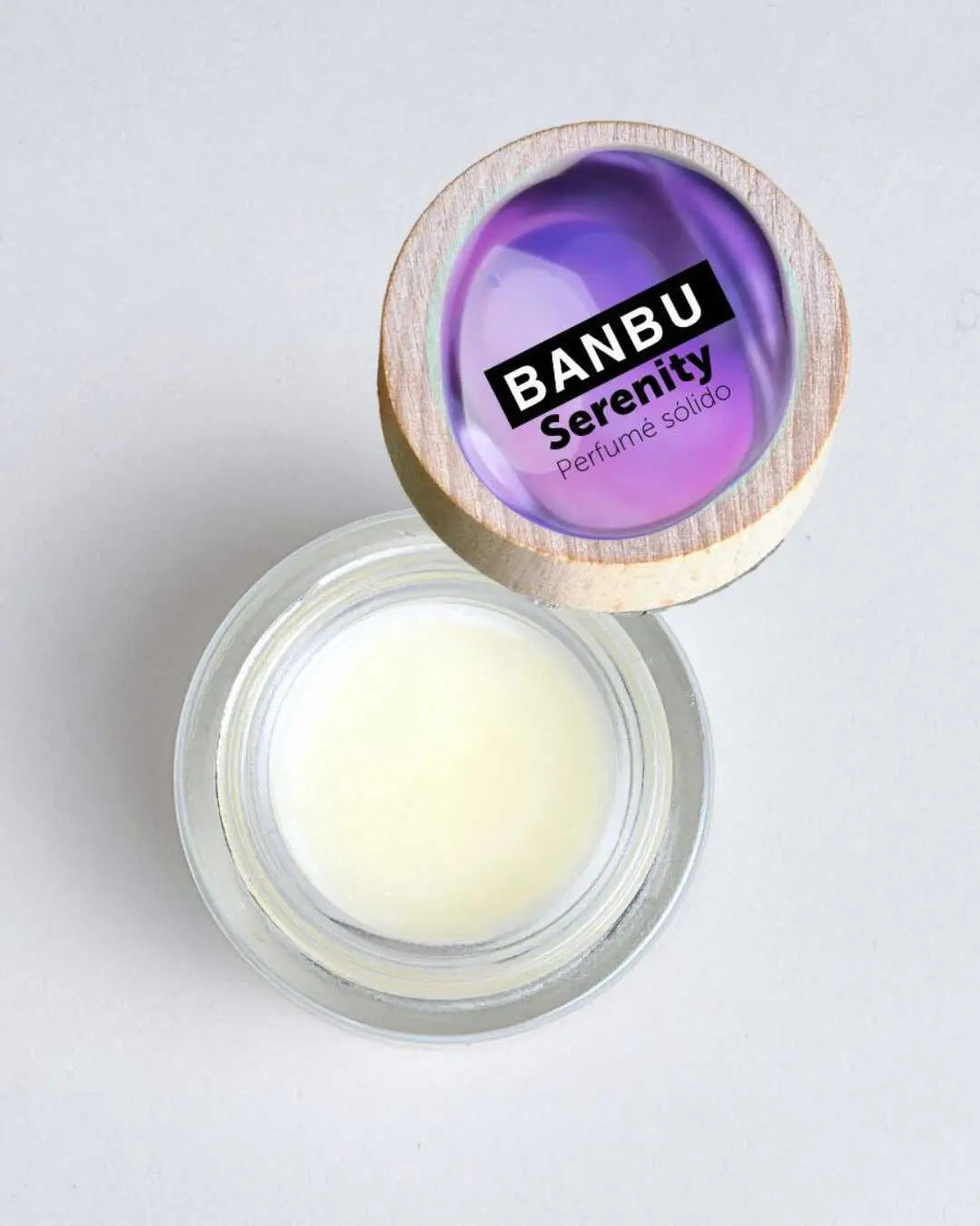 Tarro de cristal con perfume sólido Banbu Serenity y tapa de madera con detalle violeta sobre fondo gris claro.