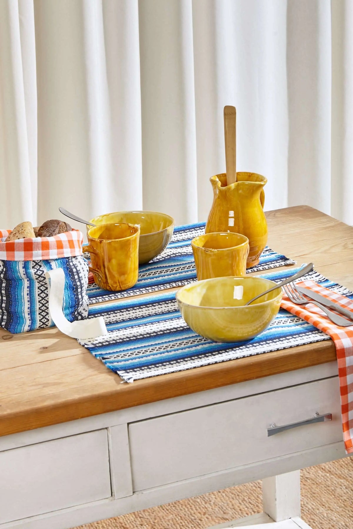 Rectangular placemat in blue, white, and black striped Alpujarra fabric pattern on a wooden table with ceramic dishware.