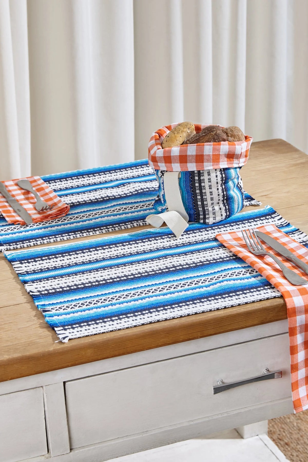 Small textile bread basket featuring blue and white Alpujarra stripes and an orange gingham inner lining.