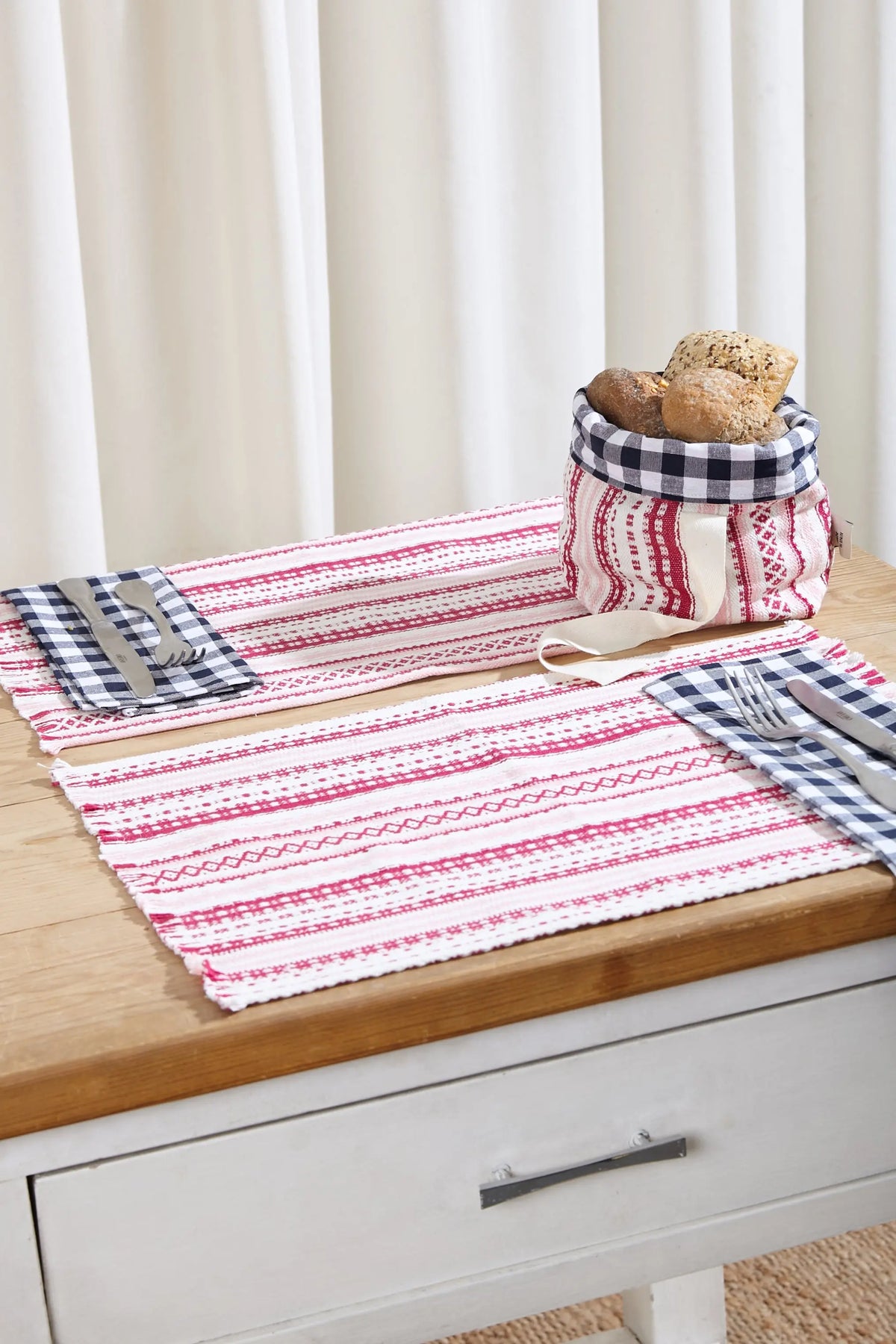 Pack de 2 manteles individuales de tela tipo alpujarra en tonos rosas con flecos, sobre mesa de madera.