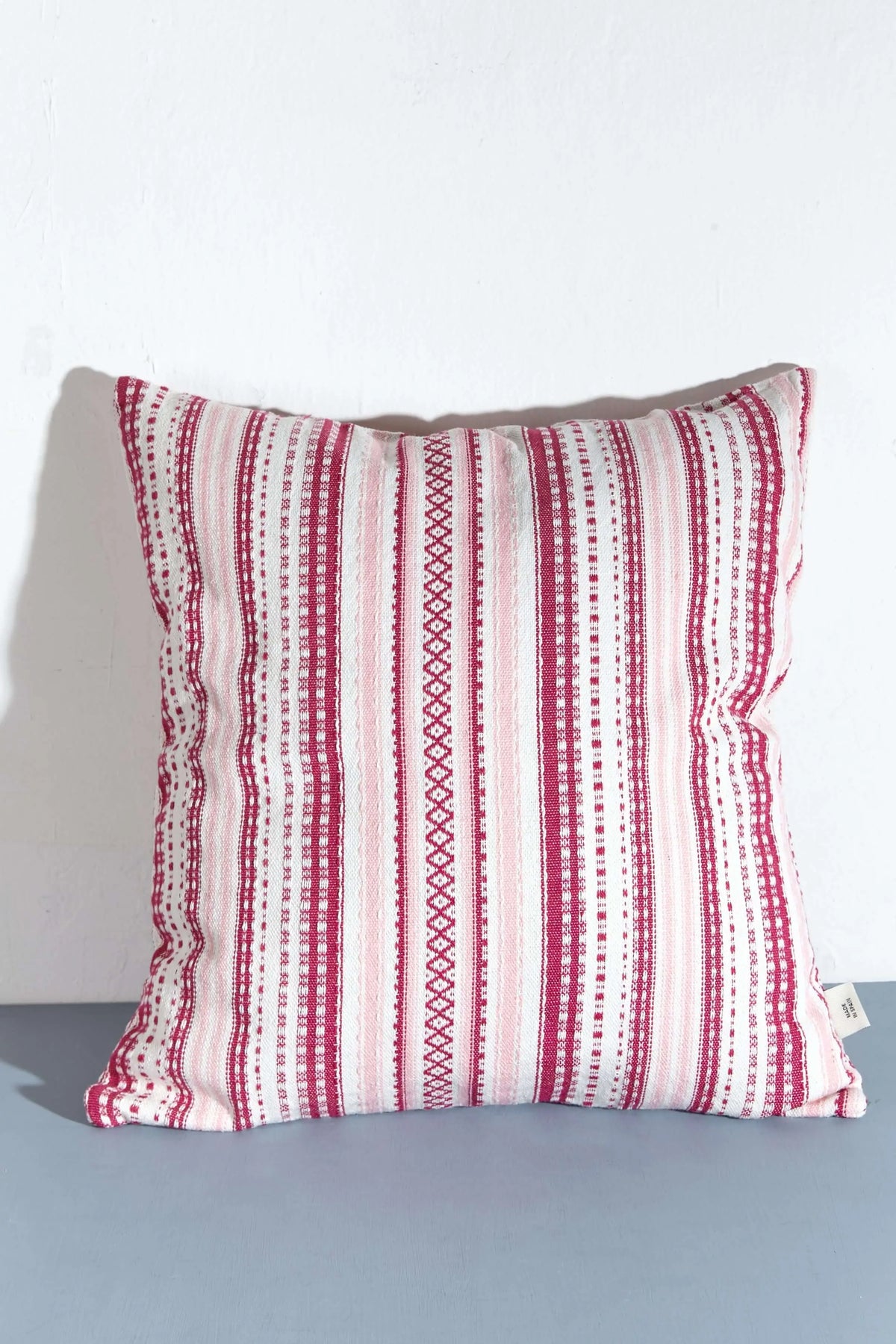 Funda de cojín cuadrada de 50x50 cm, tejido estilo alpujarra con rayas verticales en tonos rosas y blancos.