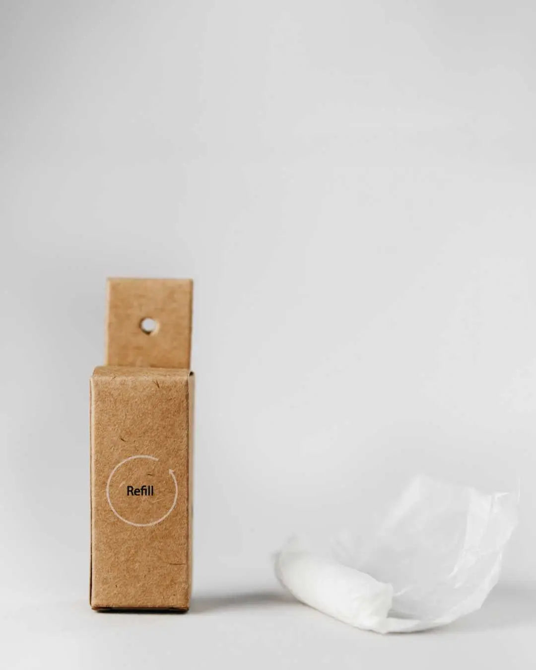 Cajita de cartón reciclado para recarga de hilo dental vegano Banbu, junto a un ovillo de hilo blanco sobre fondo gris.