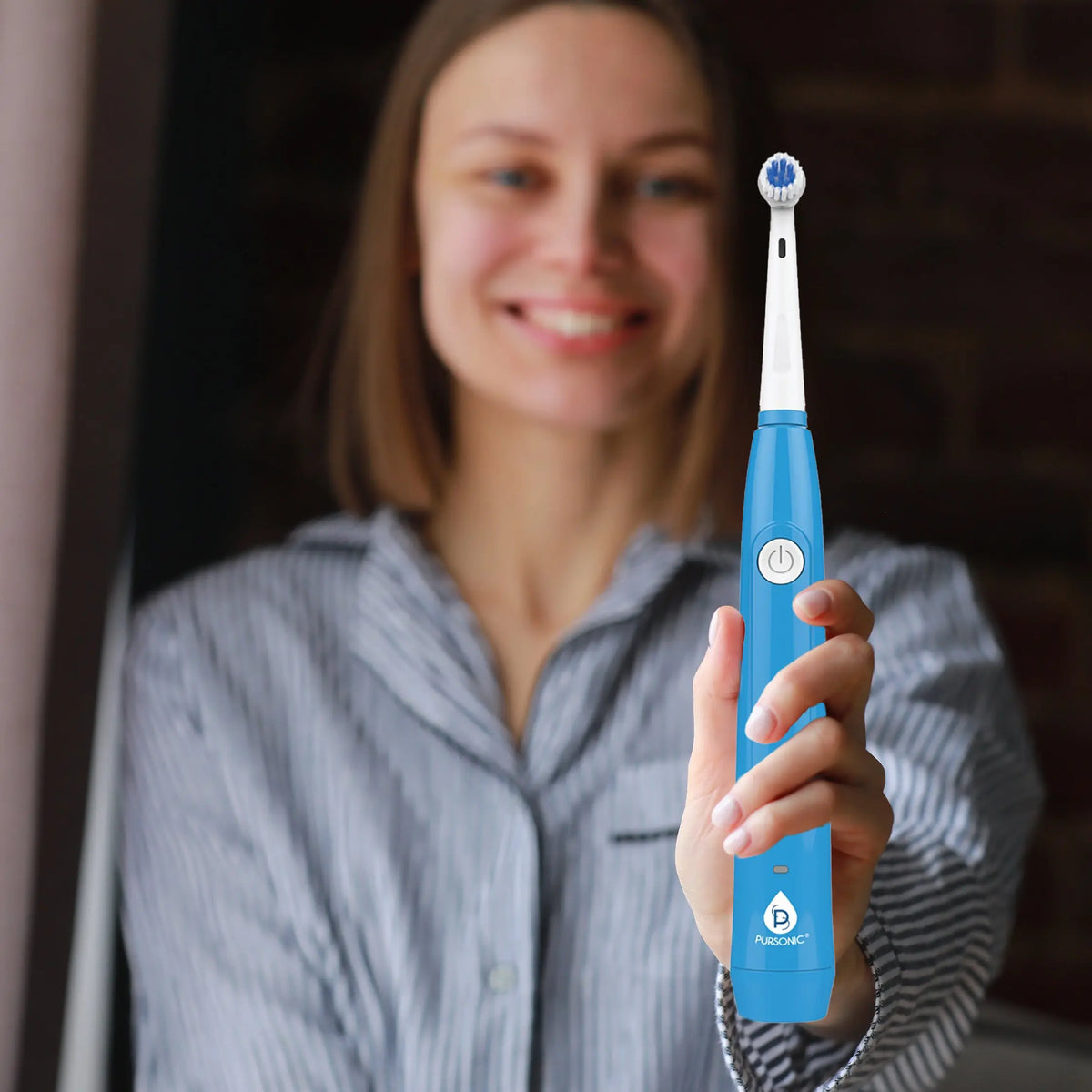 A woman holds a bright blue Pursonic rechargeable electric toothbrush with a round, white rotating brush head.