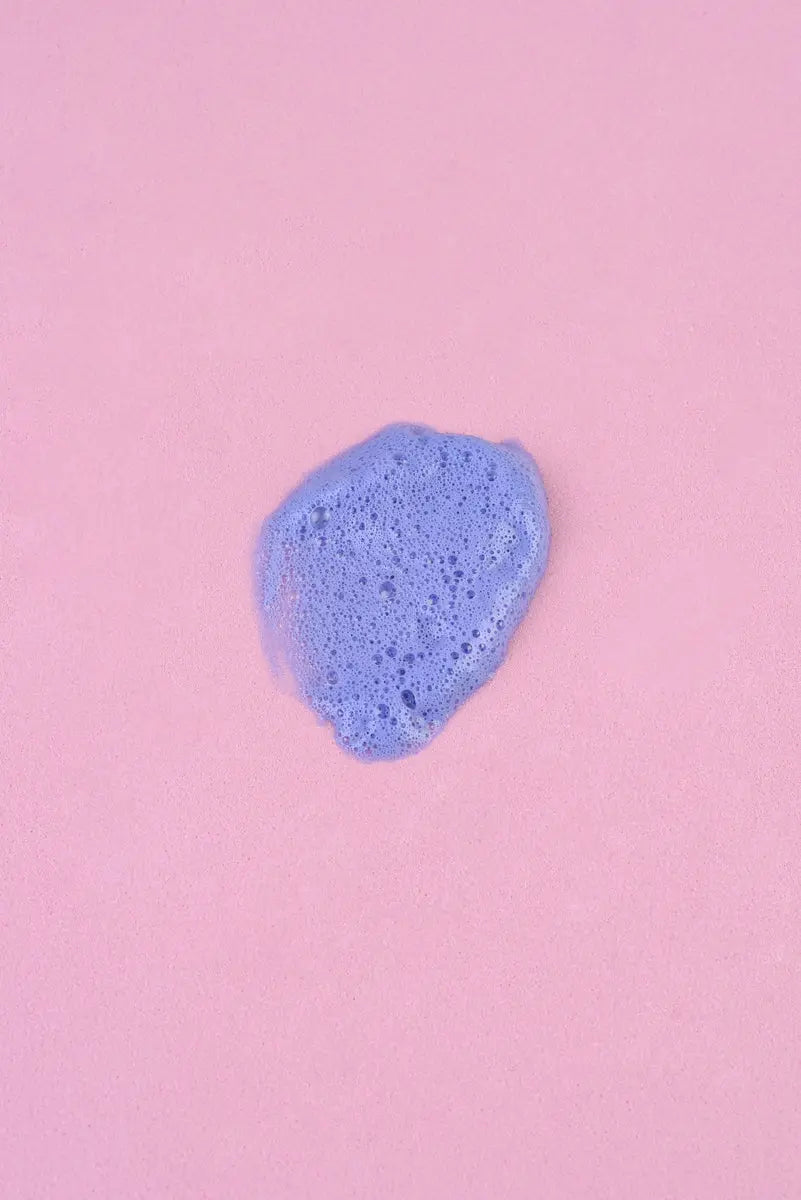 Espuma de baño color lila sobre fondo rosa, textura suave y cremosa, ideal para un momento de relajación.
