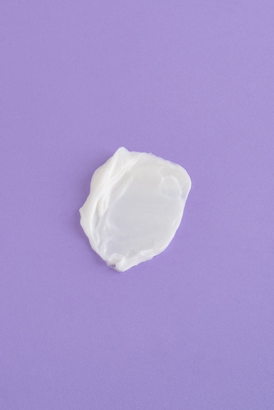 Crema hidratante blanca sobre fondo morado, textura suave y cremosa, ideal para todo tipo de piel.
