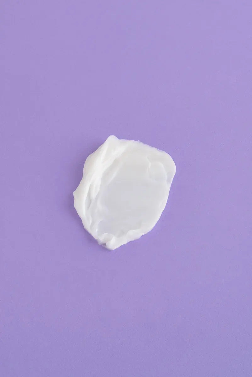 Crema hidratante blanca sobre fondo morado, textura suave y cremosa, ideal para todo tipo de piel.