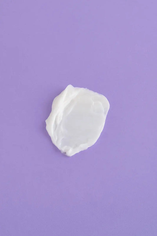 Crema hidratante blanca sobre fondo morado, textura suave y cremosa, ideal para todo tipo de piel.