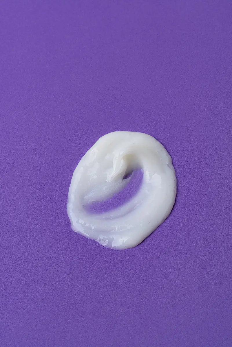 Crema hidratante blanca sobre fondo púrpura, textura suave y cremosa, ideal para el cuidado de la piel.