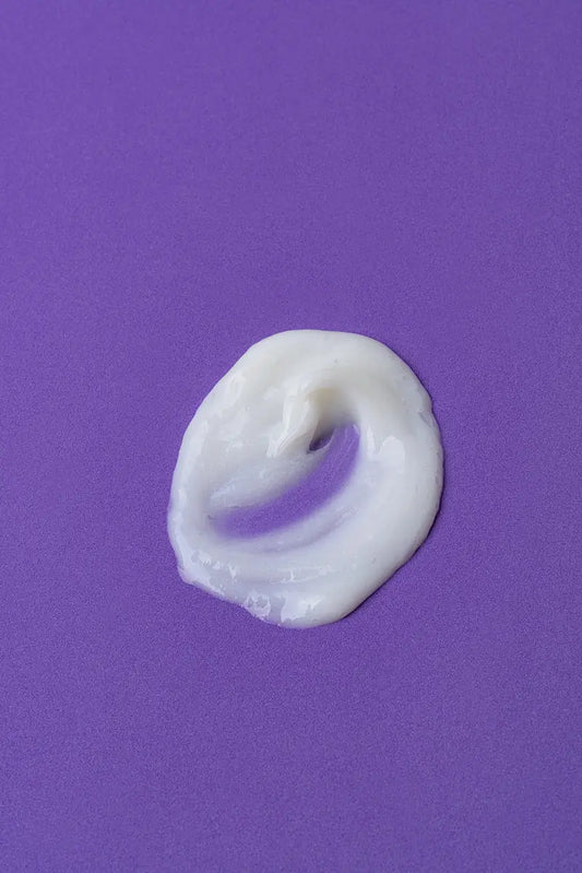 Crema hidratante blanca sobre fondo púrpura, textura suave y cremosa, ideal para el cuidado de la piel.