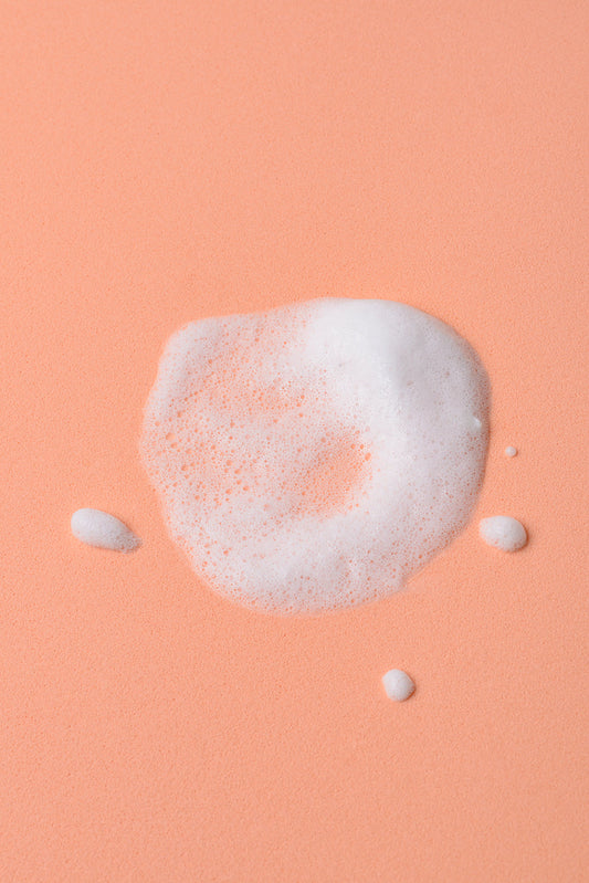 Espuma blanca sobre fondo melocotón, ideal para productos de limpieza o cuidado personal.
