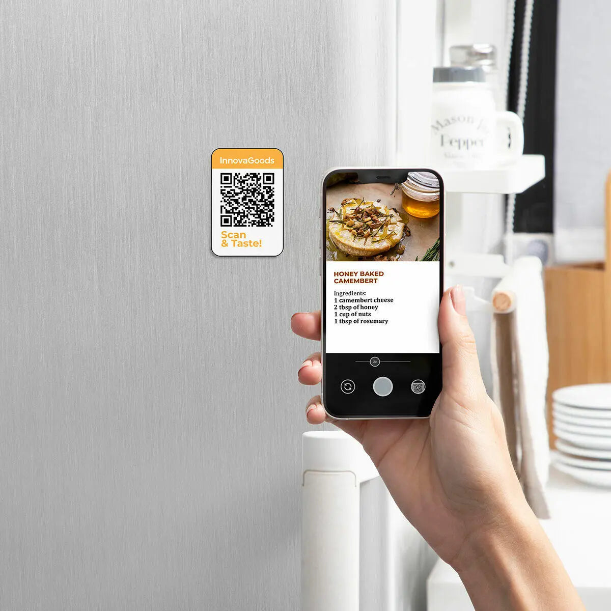 Mano sosteniendo un smartphone escaneando un código QR adhesivo en una nevera que muestra una receta de camembert.