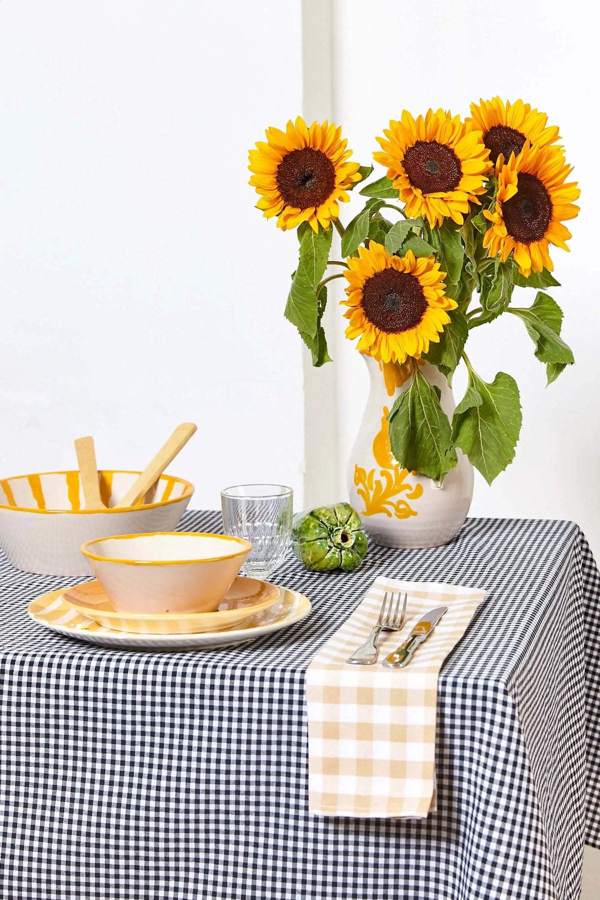 Mantel de tela con estampado de cuadros vichy en color negro sobre una mesa decorada con vajilla y girasoles.