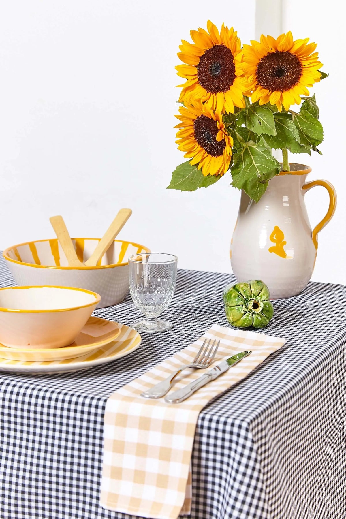 Mantel de tela con estampado de cuadros vichy en color negro sobre una mesa puesta con vajilla y un jarrón de girasoles.