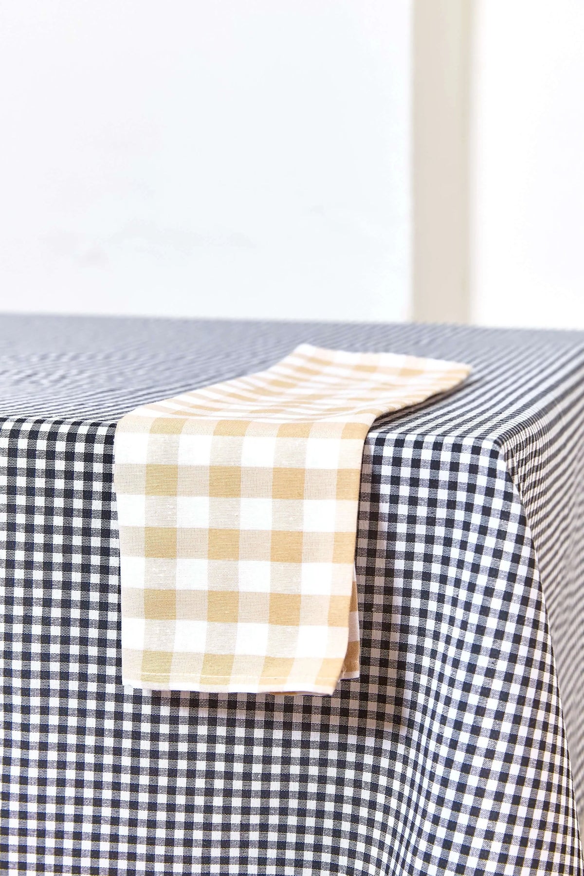 Mantel textil de cuadros vichy en negro y blanco, con una servilleta de cuadros color beige sobre la mesa.