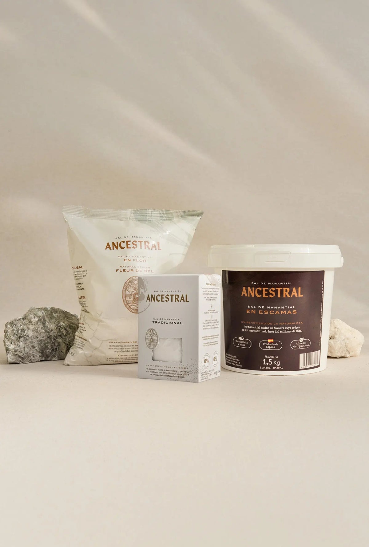 Natural spring salt set including a bag, a small box, and a white bucket, arranged with rocks on a beige background.