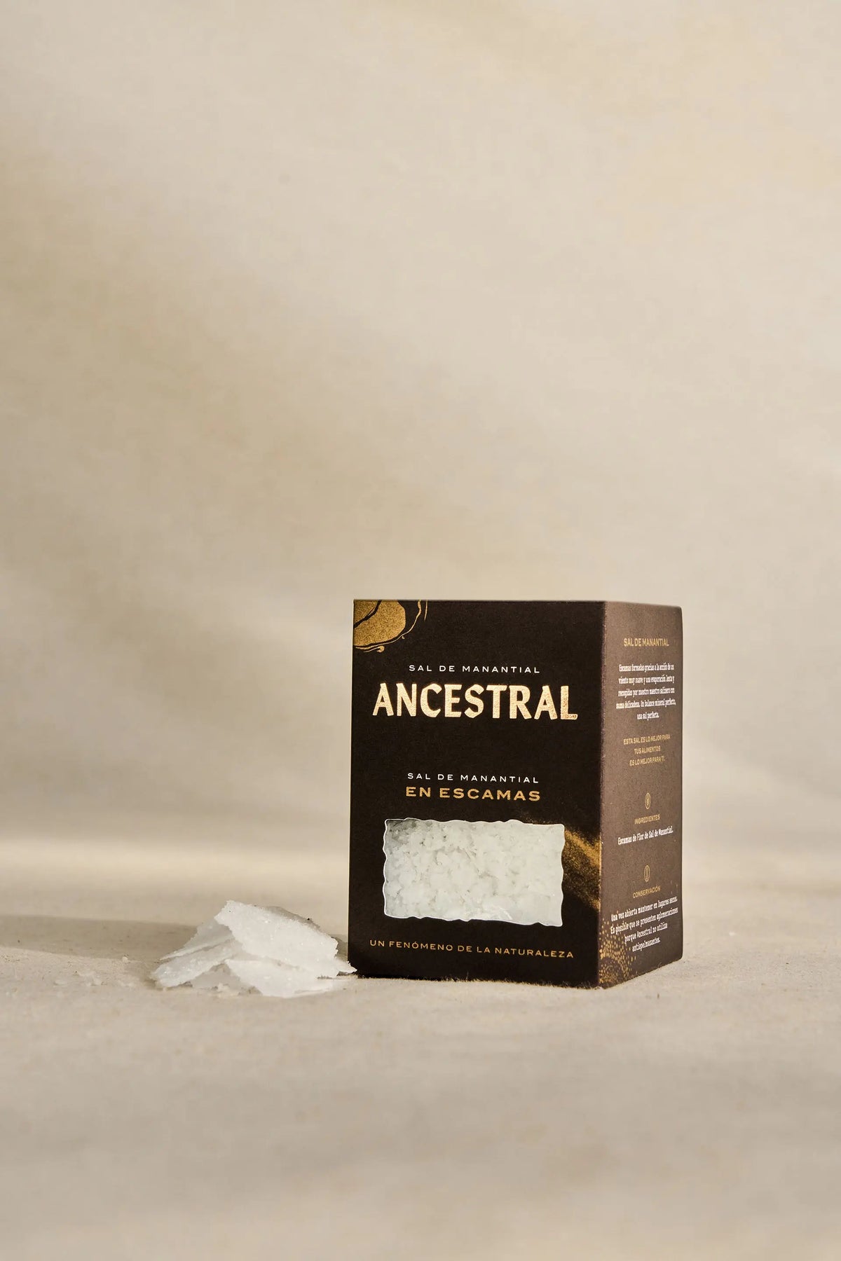 A black box of Ancestral spring salt flakes with a clear window showing white, flaky salt crystals on a beige surface.