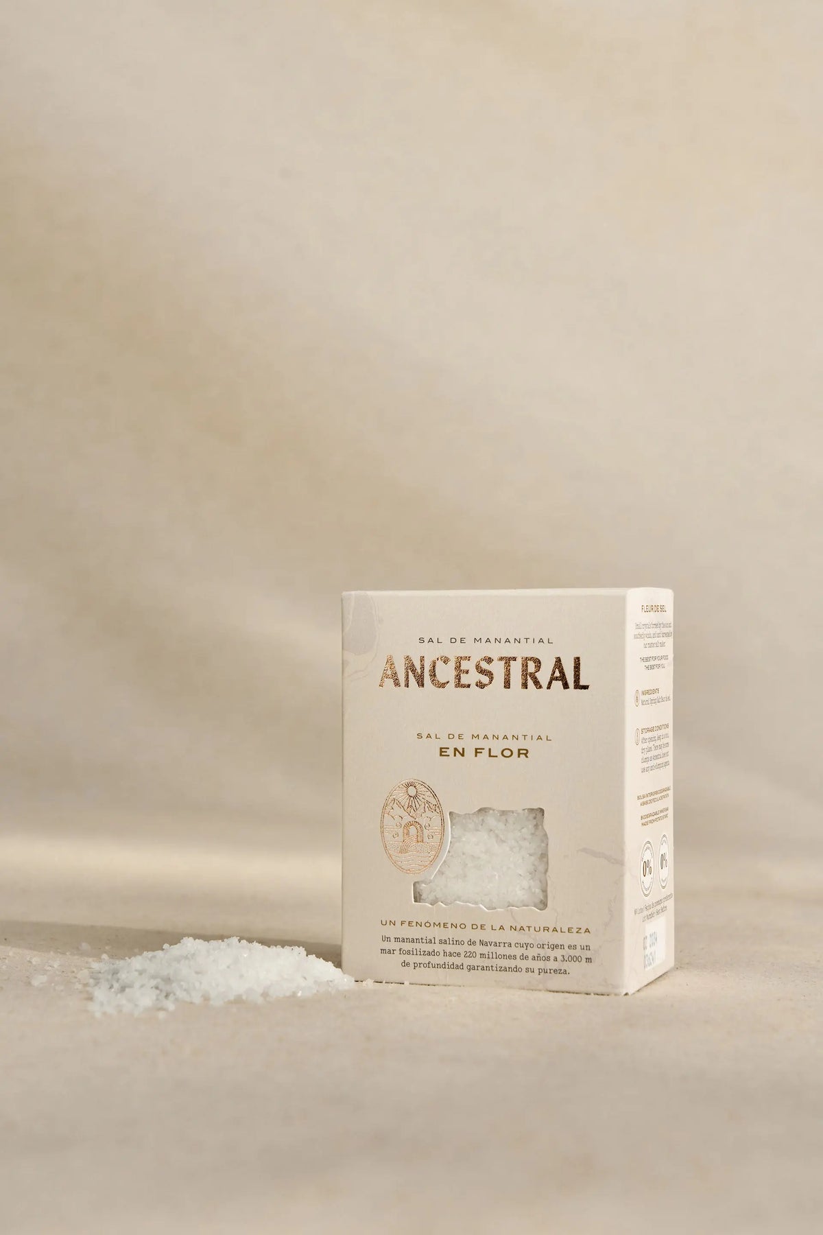 A box of Ancestral spring salt with a clear window showing white salt crystals, placed on a beige textured surface.